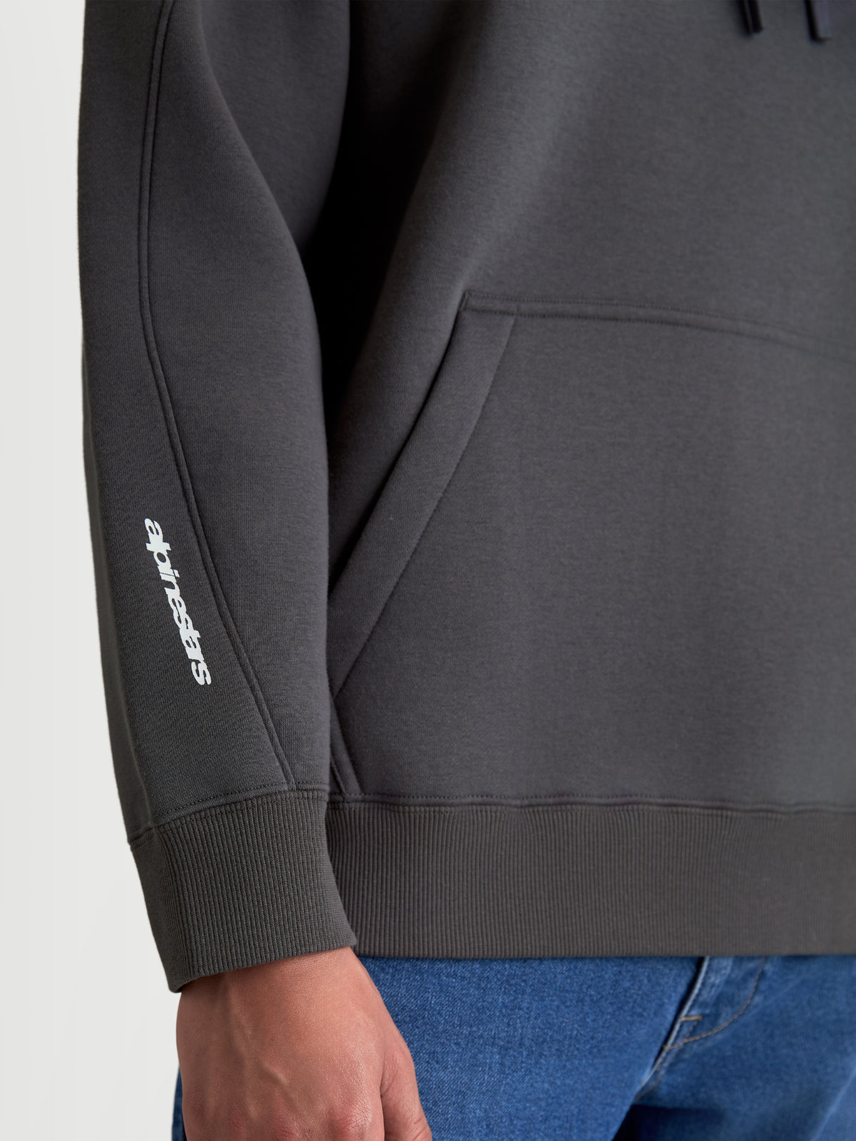 Alpinestars Prelude Oversized Hoodie, sudadera con capucha de forro polar en color gris, vista de detalle del logotipo blanco en el brazo, costuras de la manga, puño de canalé y bolsillo canguro, estilo de ropa deportiva casual