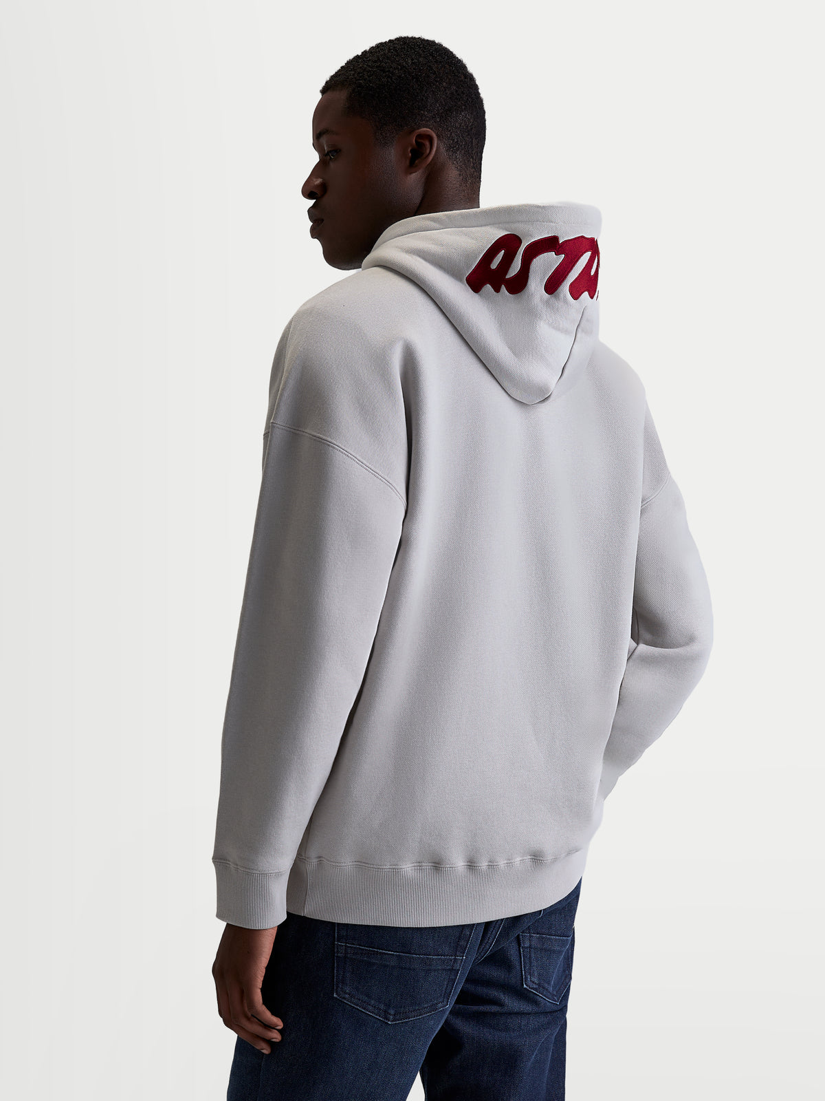 Alpinestars Sudadera Con Capucha Pioneer Oversized, sudadera sportswear de forro polar, unisex, gris cemento y rojo, ajuste oversized con logotipo bordado en rojo en la capucha, vista trasera en modelo, mezcla de algodón y poliéster reciclado