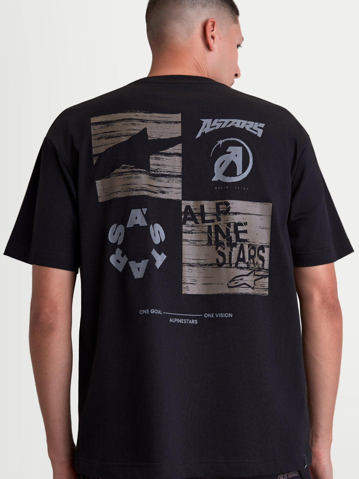 Alpinestars camiseta Checkback Oversized CSF, camiseta de mangas cortas negra, ajuste oversize, ropa deportiva de estilo casual. Vista trasera en modelo que muestra un gráfico gris grande con logotipos Astars, texto Alpinestars y el eslogan 'One Goal One Vision'.