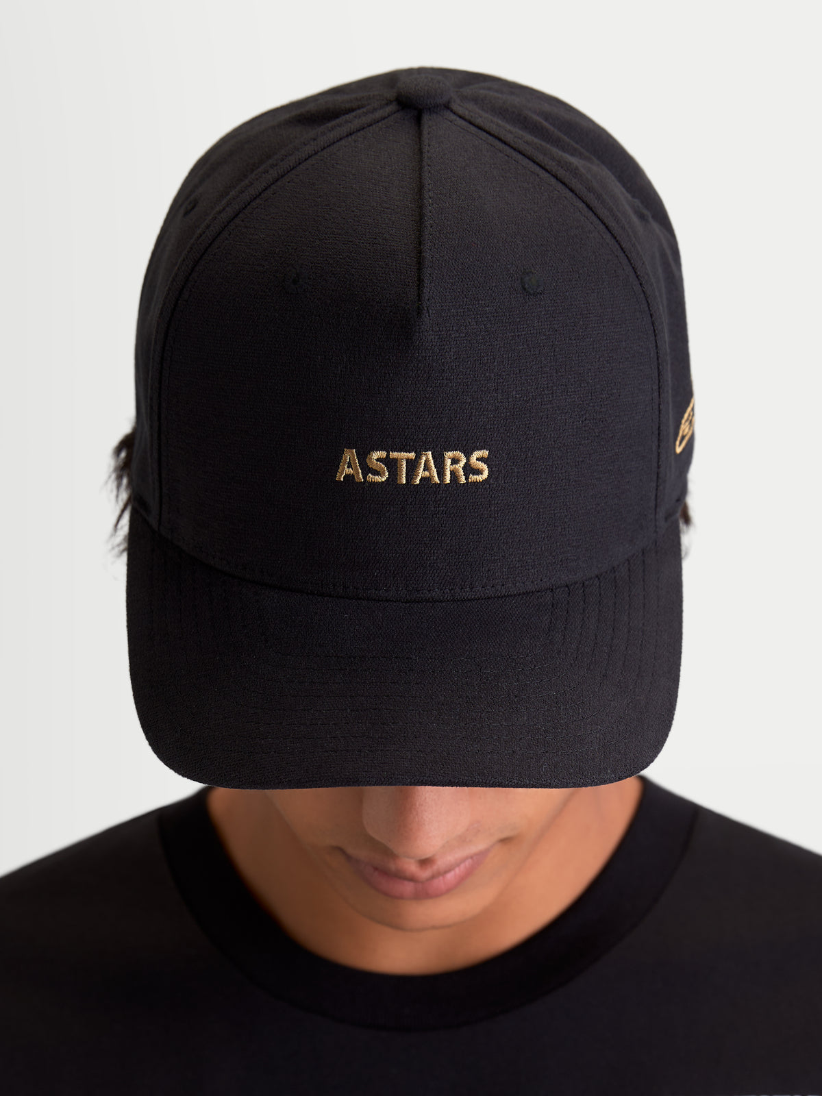 Alpinestars Gorra County Canvas, gorra de estilo motorsport para uso diario, negra con logotipo ASTARS bordado en dorado, visera curva y corona estructurada en tejido oxford peached, vista frontal en modelo
