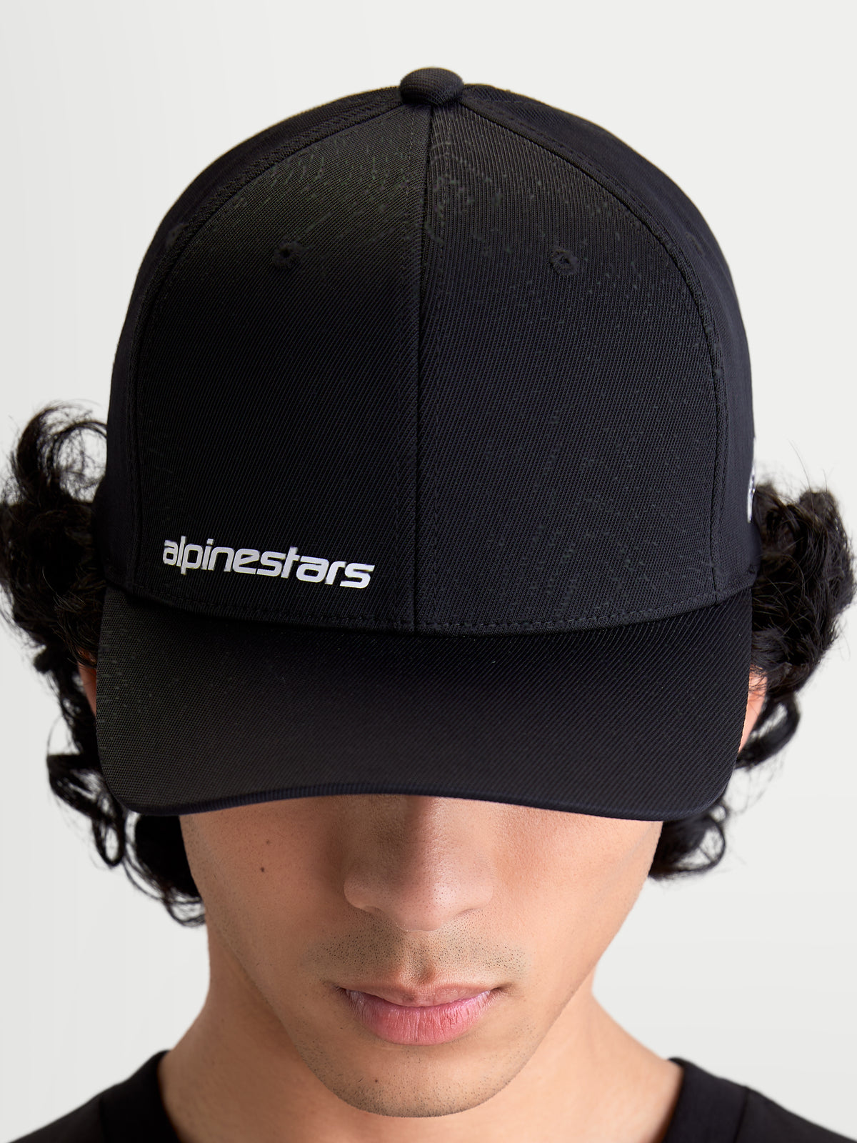 Alpinestars Gorra Points, gorra de visera curva de estilo sportswear en color negro, mostrada en un modelo, con logotipo tipográfico de Alpinestars en blanco en la parte frontal, construcción de nylon tactel ligero.