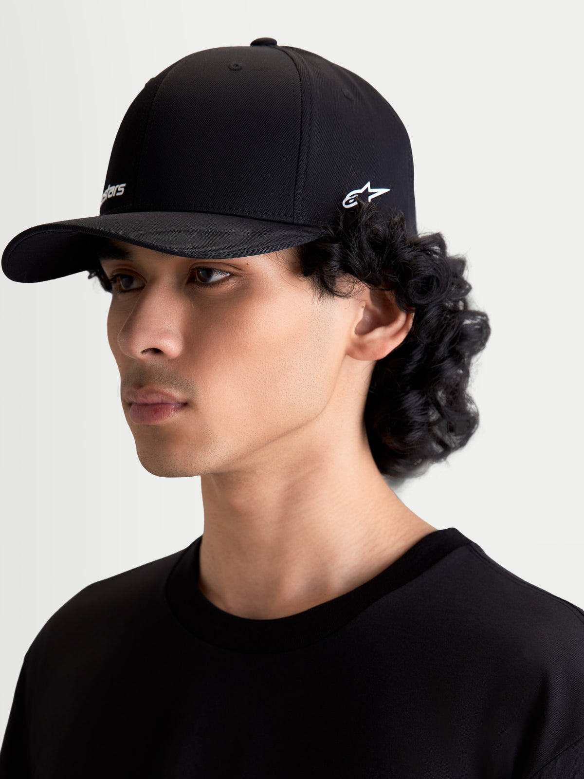 Alpinestars Gorra Points, gorra de estilo sportswear con visera curva, unisex, negra con logotipos blancos, confeccionada en nailon tactel ligero con ajuste flex-back, vista lateral en modelo, accesorio casual de lifestyle y motorsport