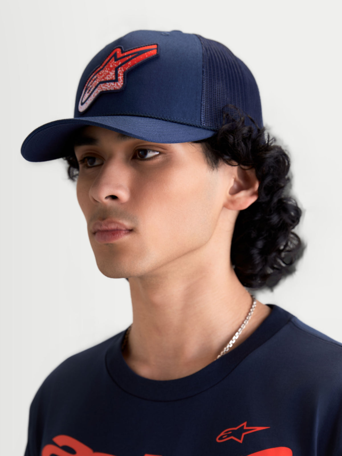 Alpinestars Gorra Meteorite, gorra de estilo trucker, azul marino y roja, visera curva y corona estructurada, panel trasero de malla, logotipo Astars con textura gravel, ropa deportiva, vista en modelo