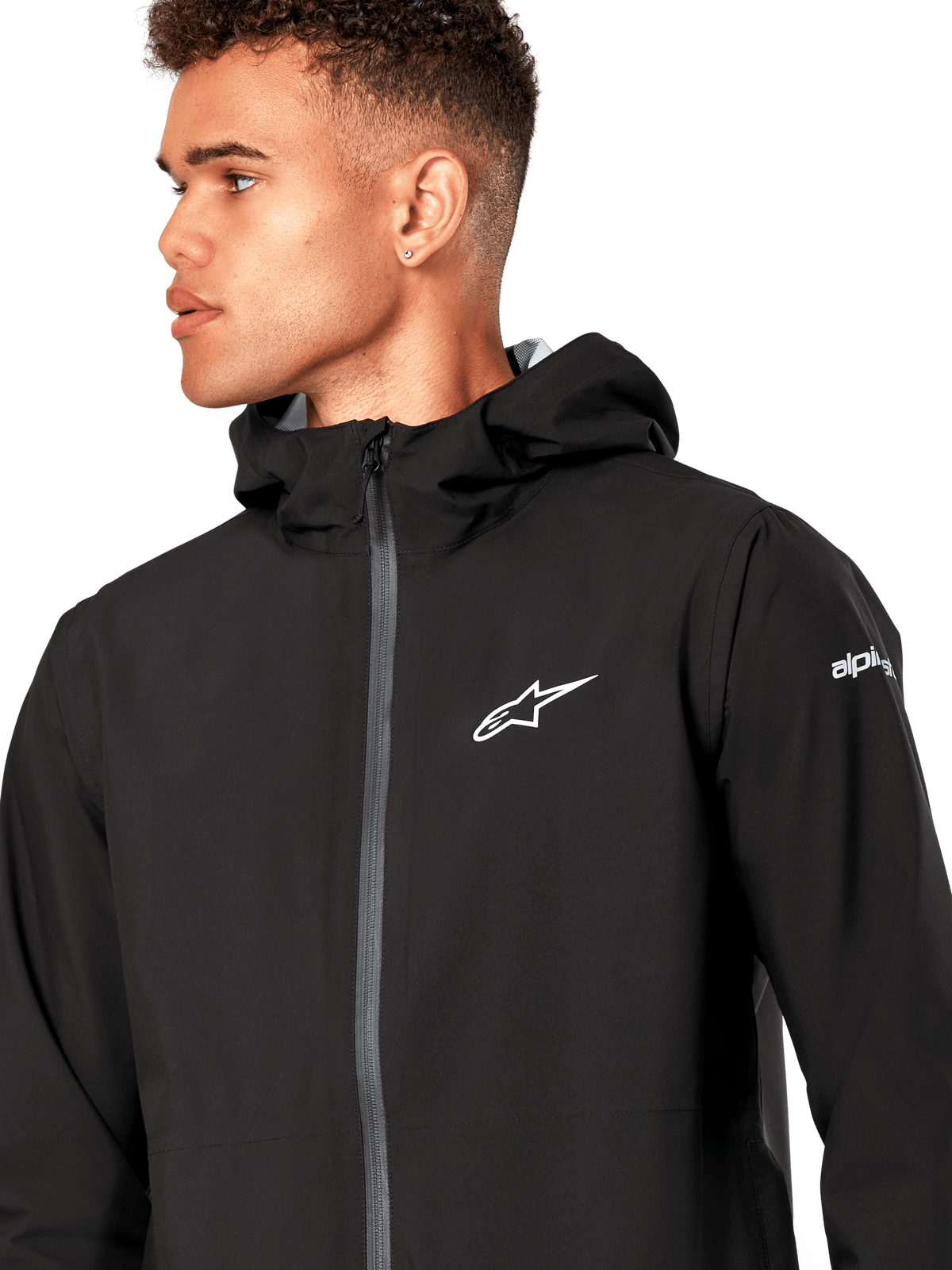 Alpinestars Kascade Rain Jacket, chaqueta impermeable negra, con logotipo de estrella blanca en el pecho, capucha fija y cremallera frontal invertida recubierta, prenda técnica casual inspirada en el automovilismo