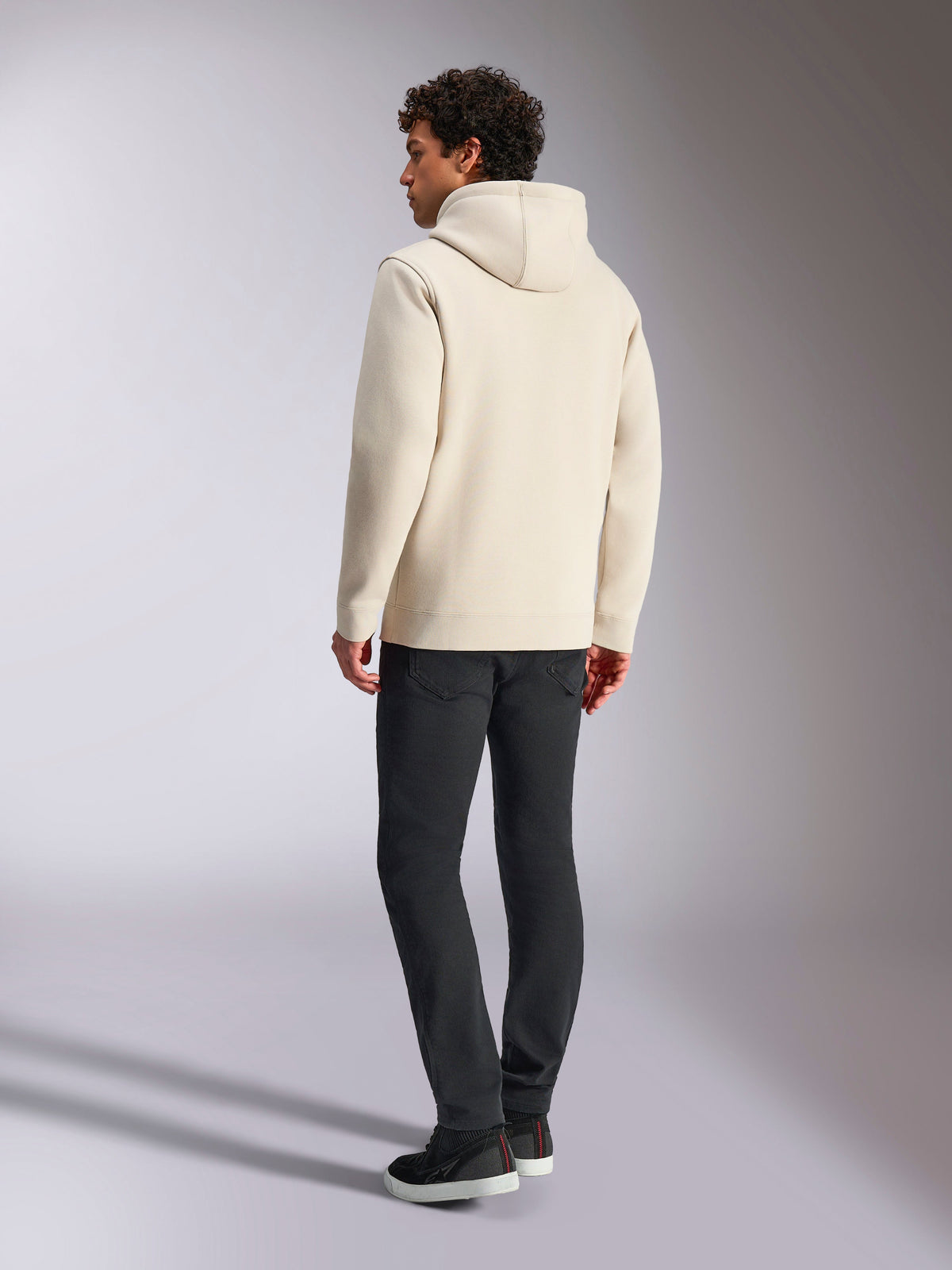 Alpinestars Always V3 Hoodie, blanco roto, vista trasera de modelo masculino con la sudadera y pantalones negros, ropa urbana informal inspirada en el automovilismo, diseño minimalista con capucha y dobladillo de canalé