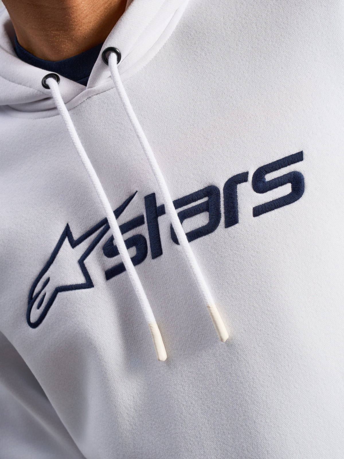 Sudadera Alpinestars Blaze V3, blanco y azul marino, primer plano del pecho con logotipo frontal impreso en azul marino y cordones blancos con puntas sumergidas, estilo casual urbano de motorsport