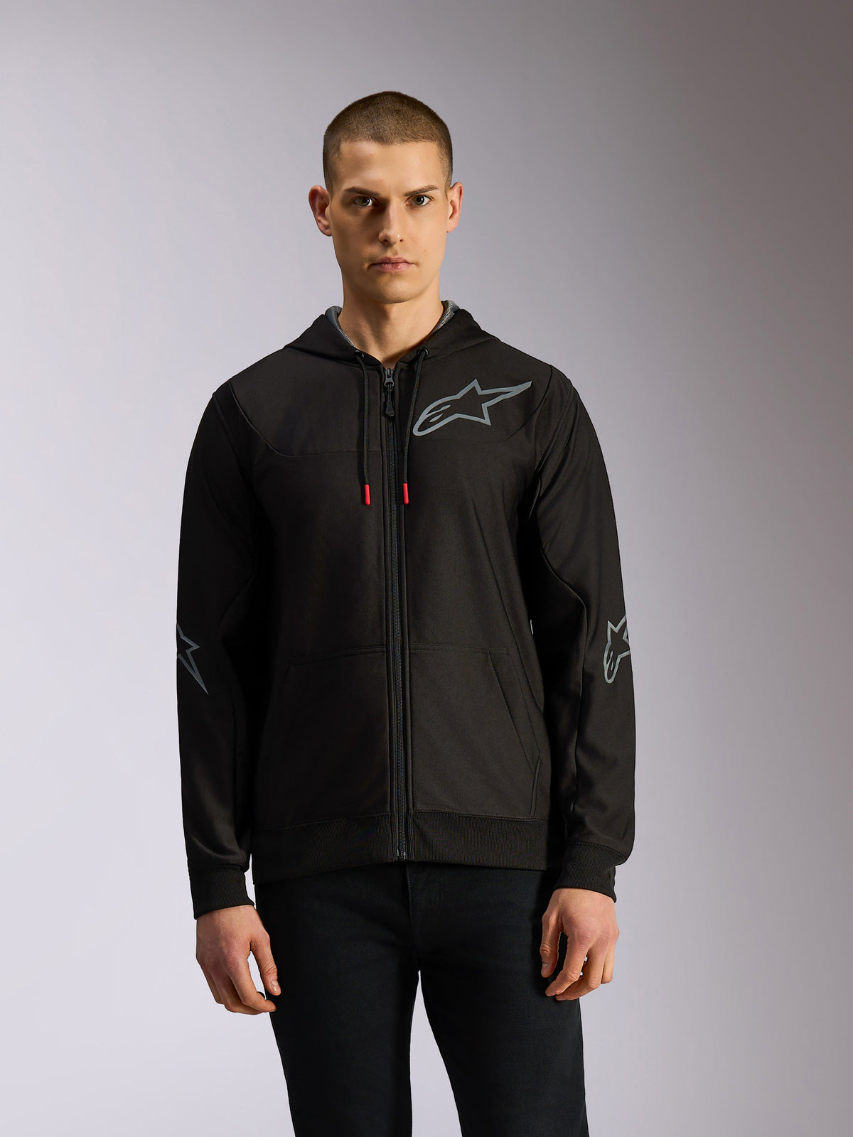 Alpinestars Sessions V3 Hoodie, sudadera de forro polar con cremallera frontal en negro y gris, con logotipos de estrella grises en el pecho y los codos, cordones técnicos con puntas rojas y estilo casual de automovilismo.
