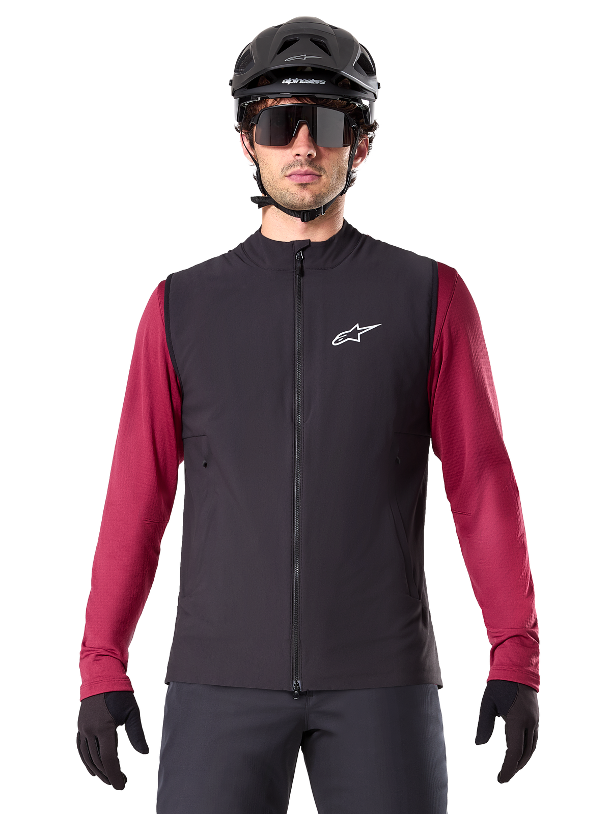 Alpinestars A-Dura Thermal Vest, chaleco de ciclismo térmico negro, usado por un modelo con un jersey granate de manga larga, casco de MTB negro y gafas de sol, con un logotipo blanco en el pecho, protección térmica ligera para ciclismo de montaña