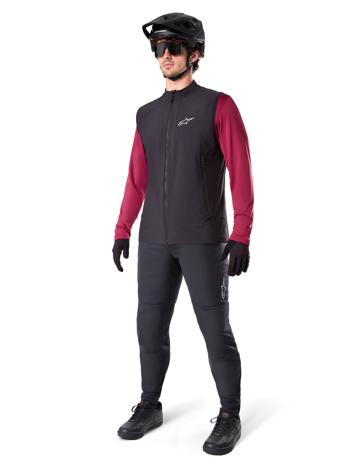 Chaleco Térmico Alpinestars A-Dura, chaleco de ciclismo negro, usado por un ciclista sobre un jersey de manga larga granate y pantalones negros, con casco de MTB y guantes negros, diseñado para ciclismo de montaña en climas fríos