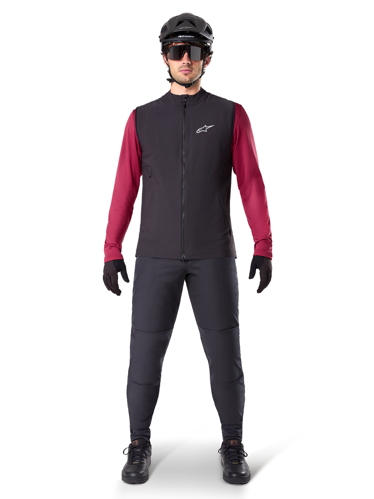 Alpinestars Chaleco Térmico A-Dura, chaleco de ciclismo negro sobre un jersey granate de manga larga, combinado con pantalones de MTB gris oscuro, casco y gafas de sol negras, ropa técnica de bicicleta de montaña para climas fríos