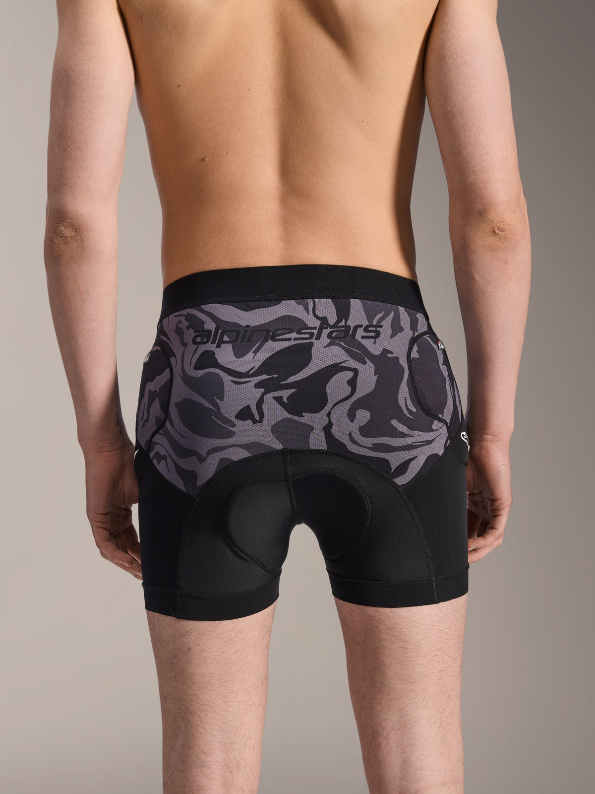 Alpinestars A-Motion Plasma Protection Boxers, shorts de protección para MTB, Black Camo, vista trasera mostrada por un modelo, con el logotipo de Alpinestars en un panel de malla de camuflaje, badana integrada y bolsillos de protección en la cadera, capa base transpirable para ciclismo off-road