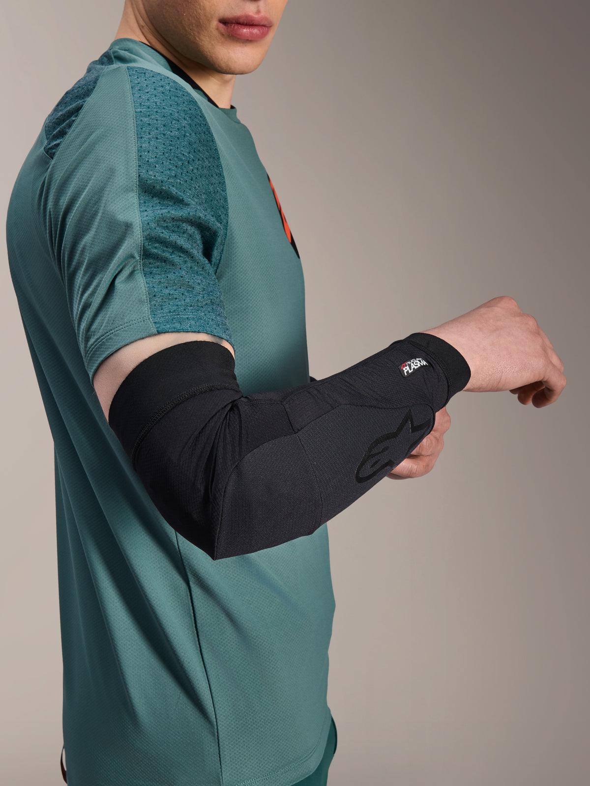 Manga de codo Alpinestars A-Motion Plasma, protector de codo para ciclismo, negro, usado por un ciclista con jersey verde azulado, con el logotipo de Alpinestars y la marca Nucleon Plasma, diseño estilizado y transpirable para protección de MTB