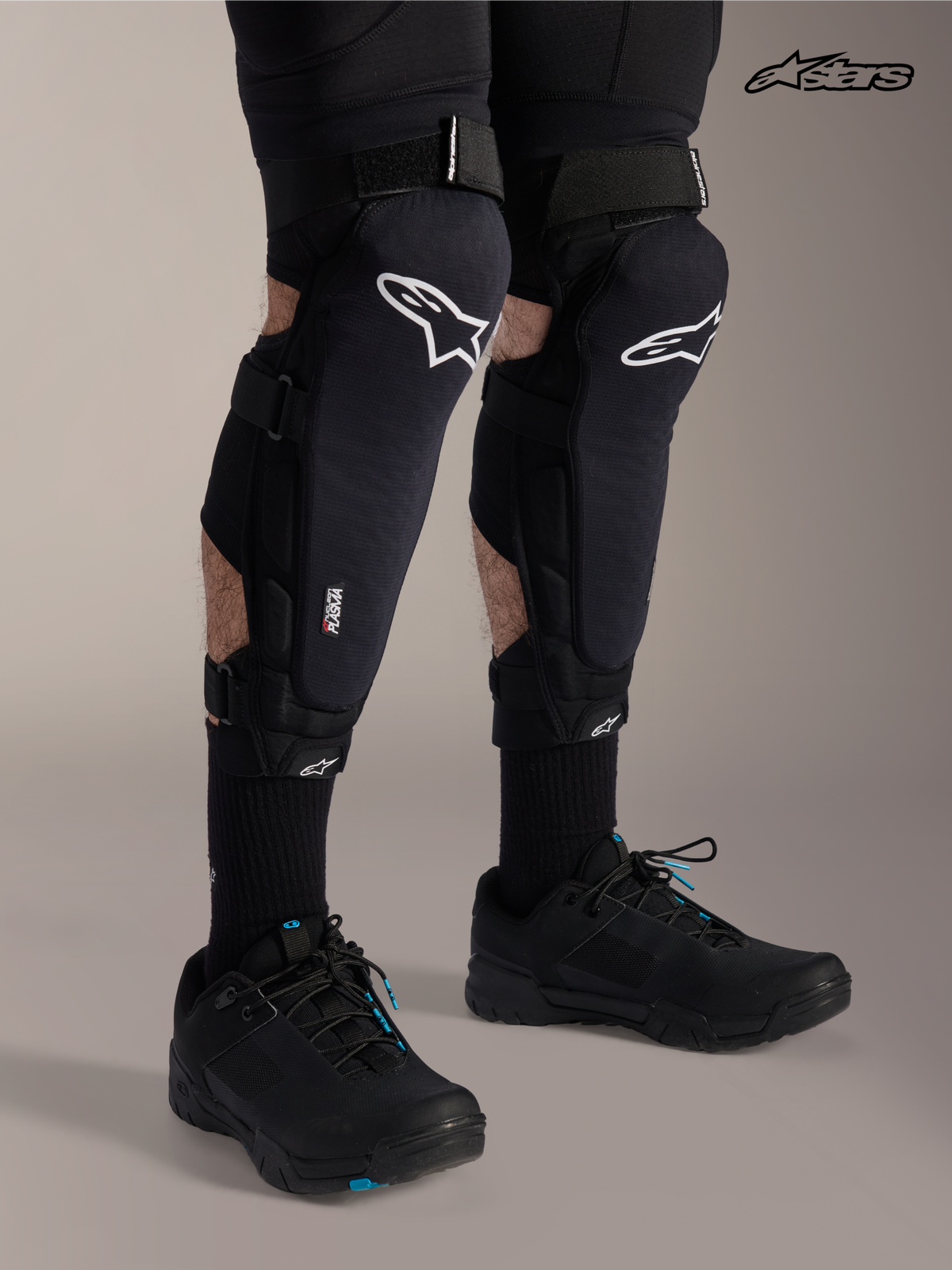 Alpinestars A-Impact Plasma Pro, protectores de rodilla y espinilla para bicicleta de montaña, negros con logotipo blanco, vista frontal en modelo con sistema de triple correa y protección Nucleon Plasma
