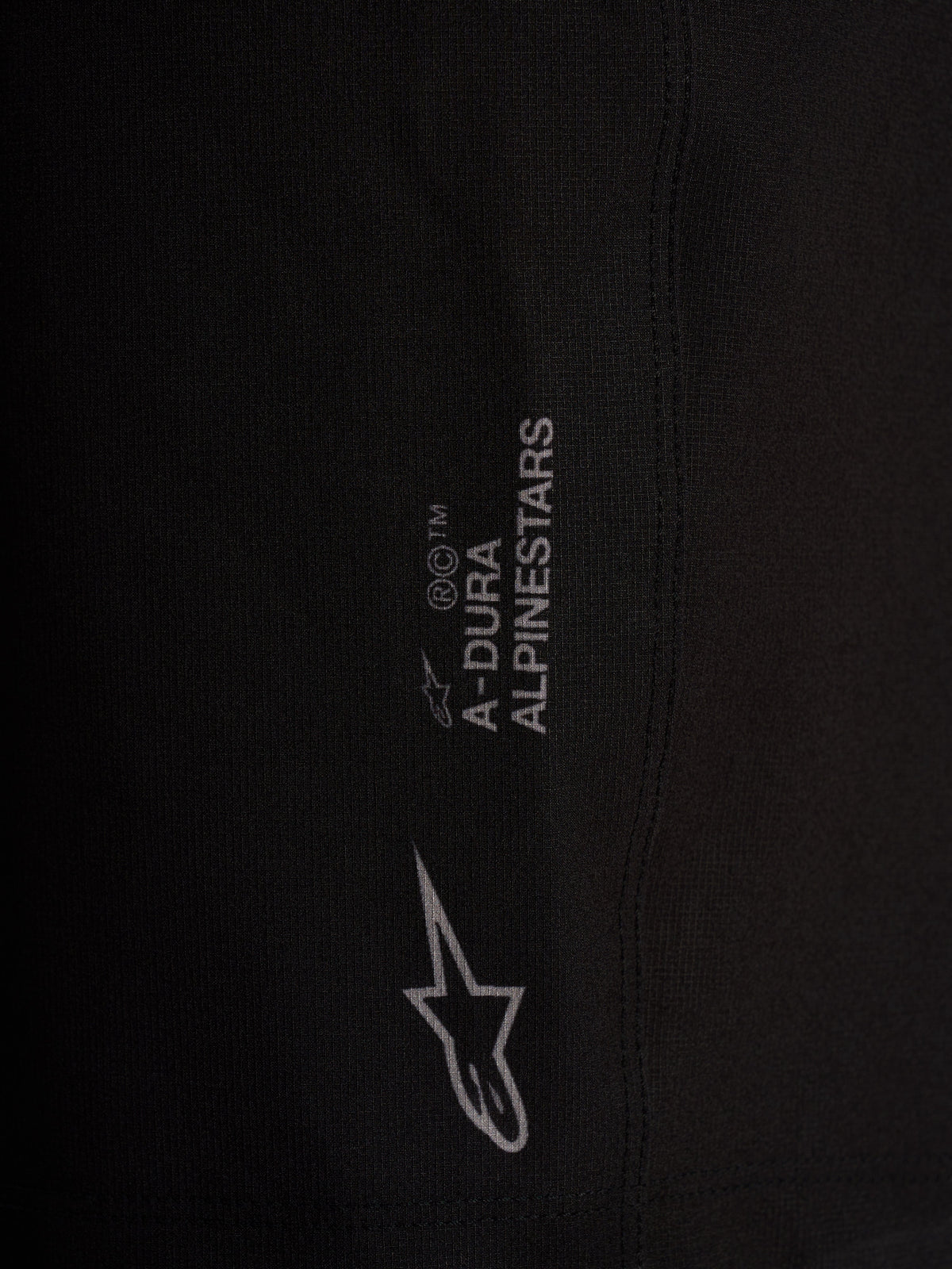 Detalle de pantalones Alpinestars A-Dura Ride negros, logotipos blancos y tejido elástico de alto rendimiento