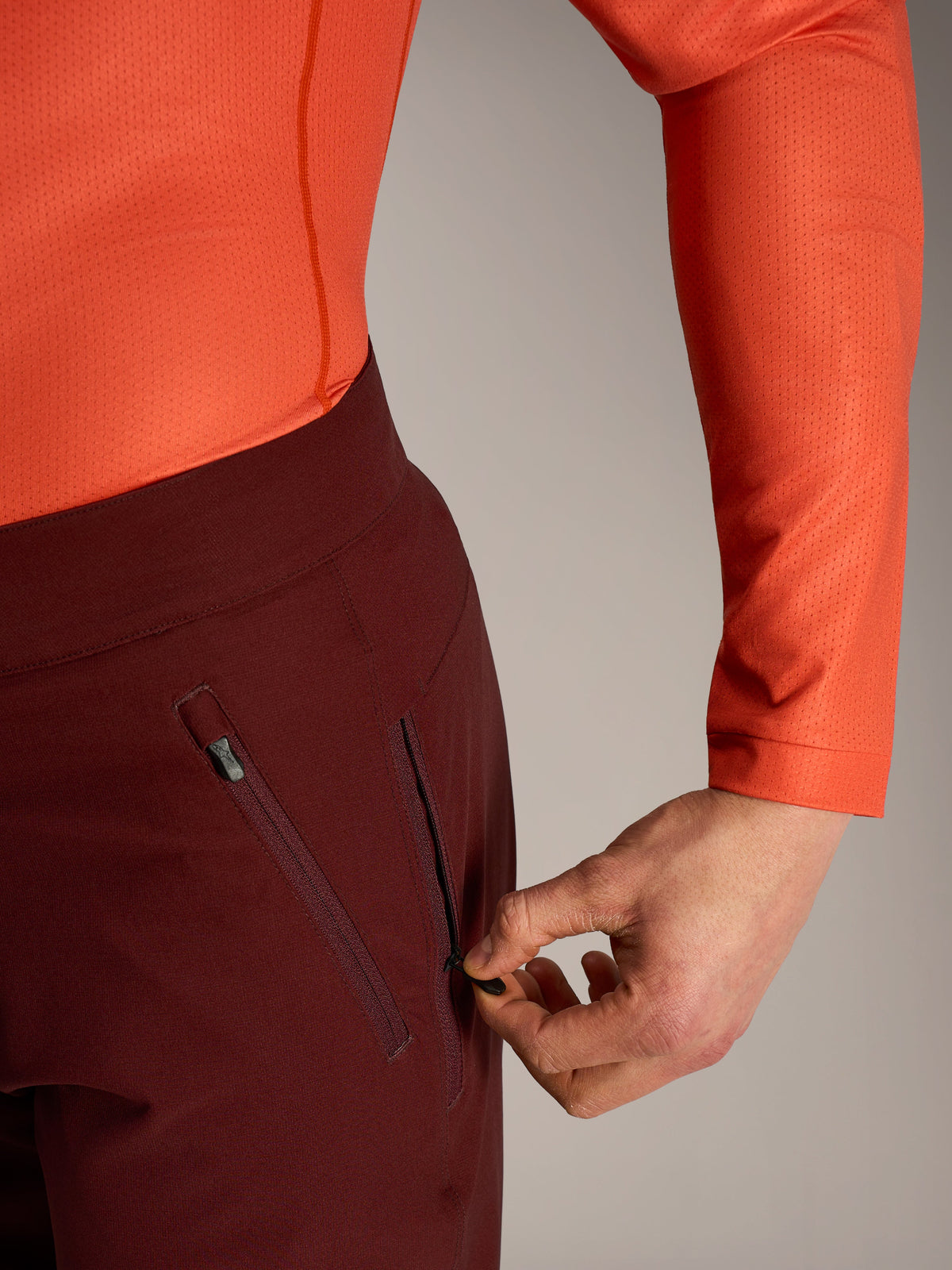 Pantalones cortos Alpinestars A-Dura Ride en bordeaux, detalle de mano abriendo el bolsillo lateral con cremallera.