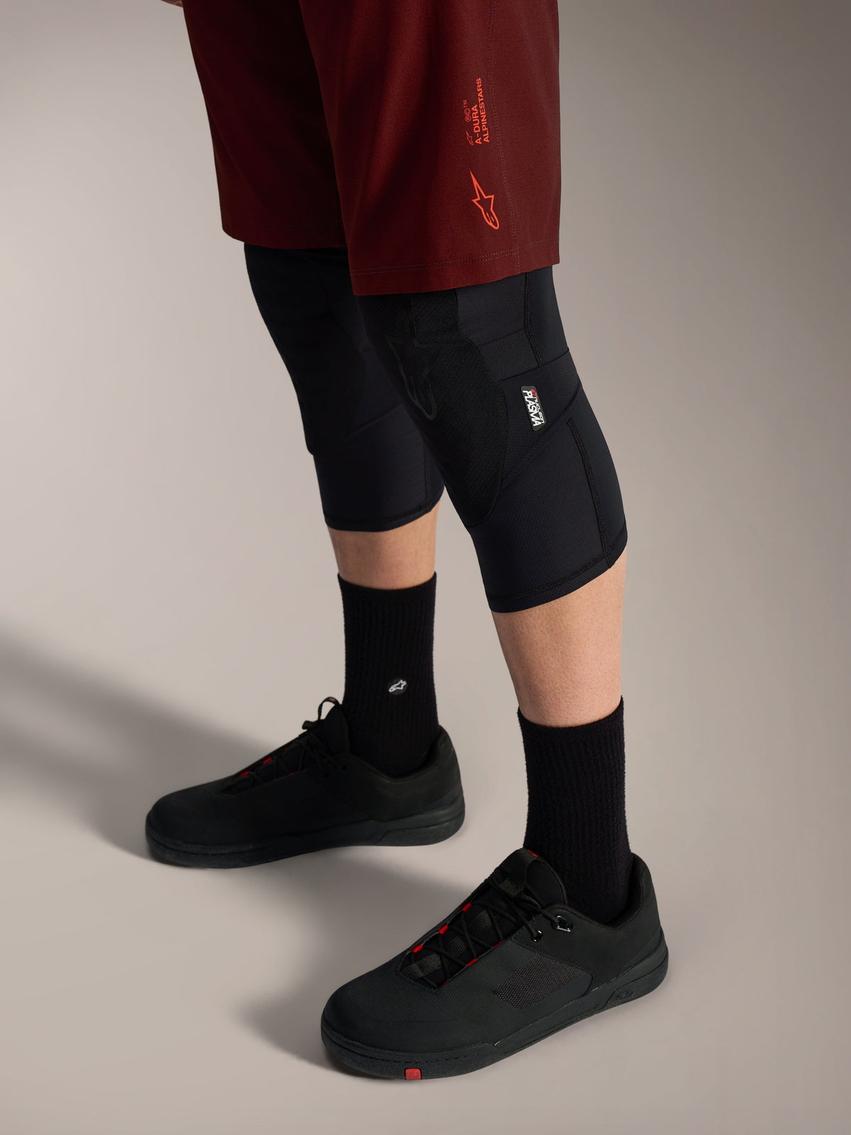 Pantalones Alpinestars A-Dura Ride burdeos, shorts de MTB elásticos con logotipo distintivo, rodilleras y calzado negros.