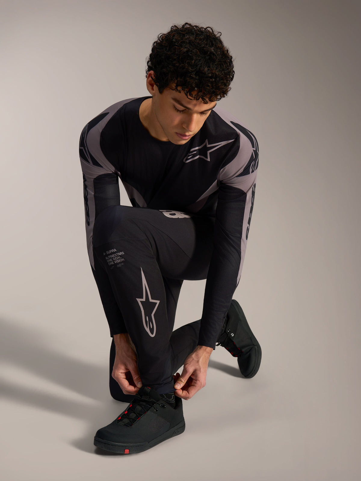 Pantalones Alpinestars A-Supra Elite negros con logotipos grises, modelo arrodillado para MTB de alto rendimiento.
