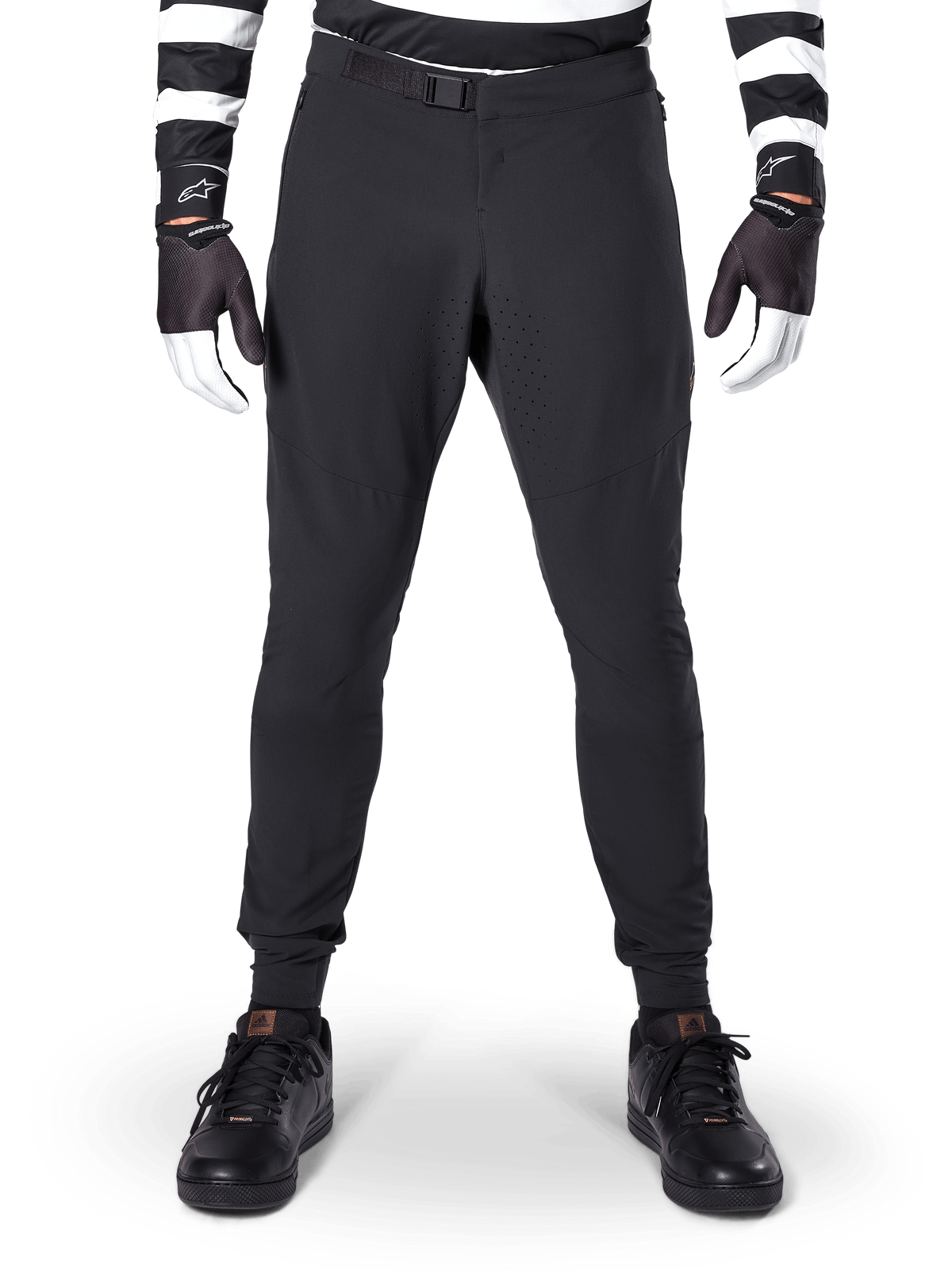 Alpinestars A-Aria Elite Pants, pantalones de MTB en color negro, vista frontal que muestra las perforaciones láser y el cierre de hebilla magnética, usados con jersey de rayas blancas y negras y guantes negros, equipamiento de ciclismo de alto rendimiento para senderos