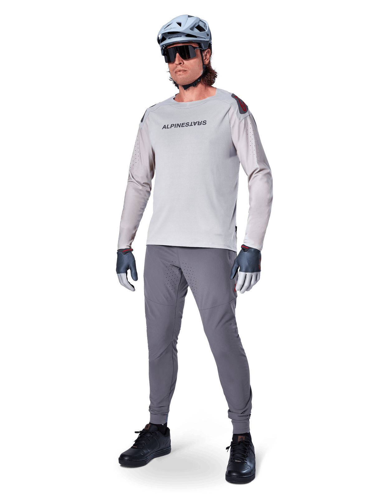 Pantalones Alpinestars A-Aria Elite, pantalones de MTB gris oscuro, usados por un ciclista con jersey de manga larga gris claro y casco gris, con perforaciones láser para ventilación en los muslos y ajuste de rendimiento cónico para ciclismo de montaña