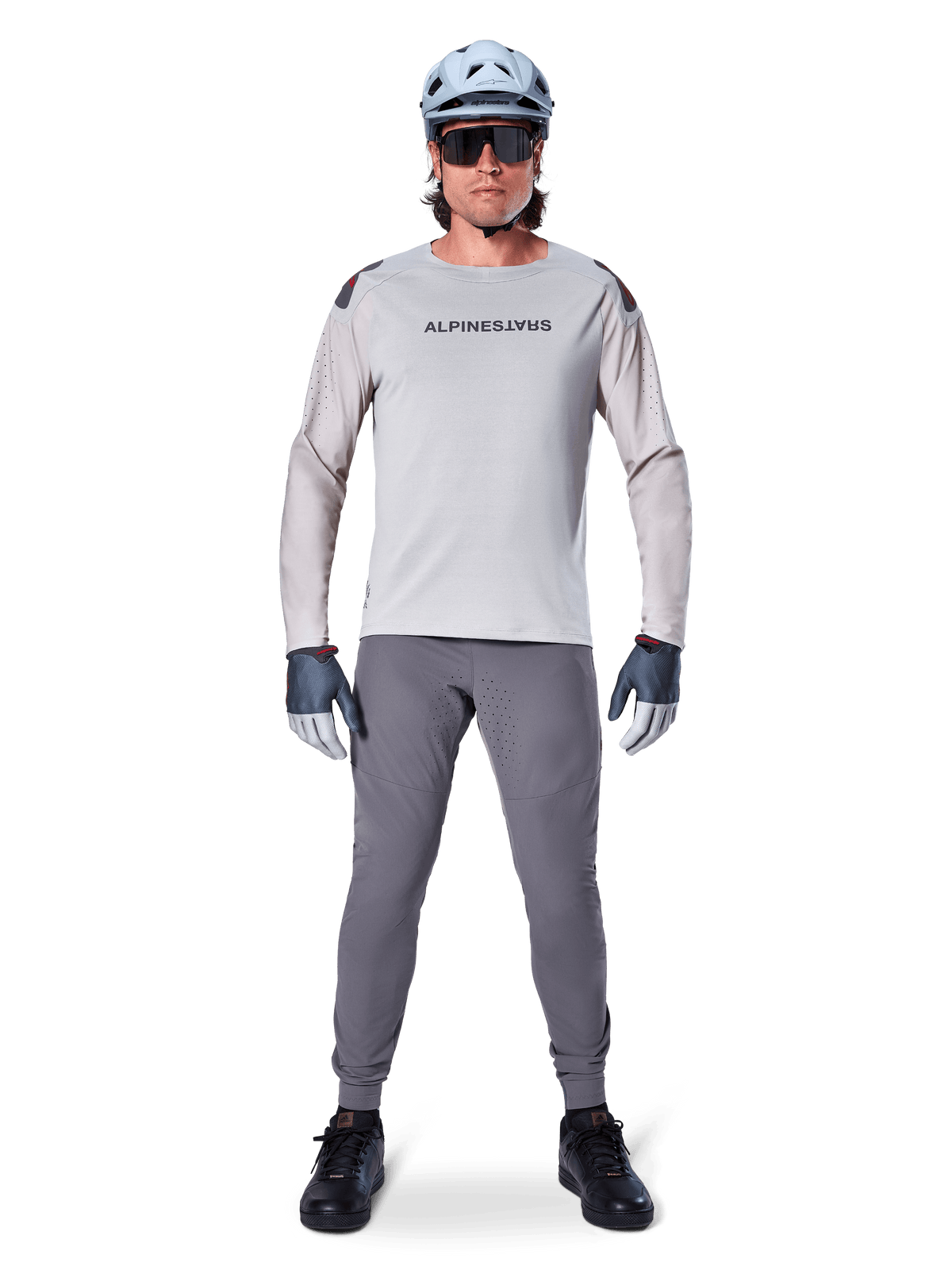 Pantalones Alpinestars A-Aria Elite, pantalones de ciclismo de montaña gris oscuro, usados por un ciclista con jersey de manga larga gris claro, casco azul claro y calzado negro, con perforaciones láser visibles en la parte interna de las piernas y un ajuste de rendimiento entallado
