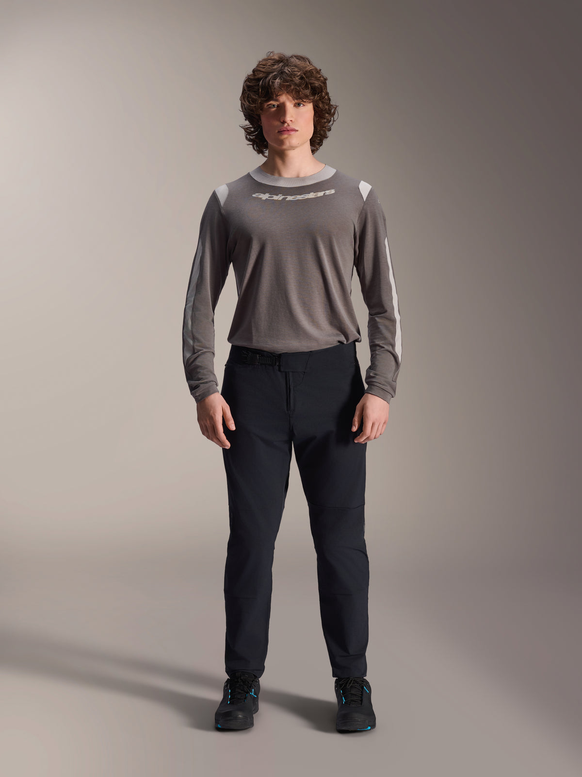 Pantalones Alpinestars A-Dura Elite, pantalones negros para bicicleta de montaña, ropa técnica de ciclismo con un ajuste regular, combinados con un jersey gris de manga larga y zapatillas negras, construcción duradera en Cordura® para recorridos fuera de pista