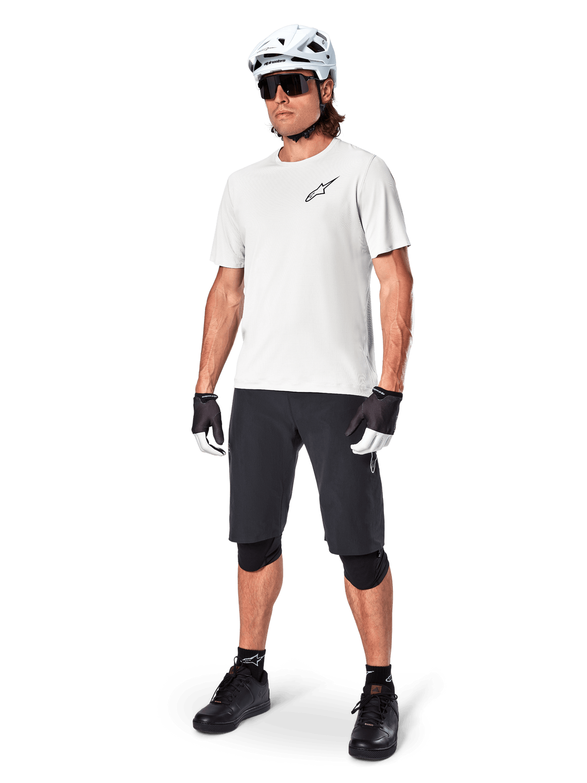 Male mountain biker wearing Alpinestars A-Aria Shorts, Black cycling shorts, styled with a white short-sleeve jersey, white mountain bike helmet, and black performance gear, full outfit for off-road trail riding