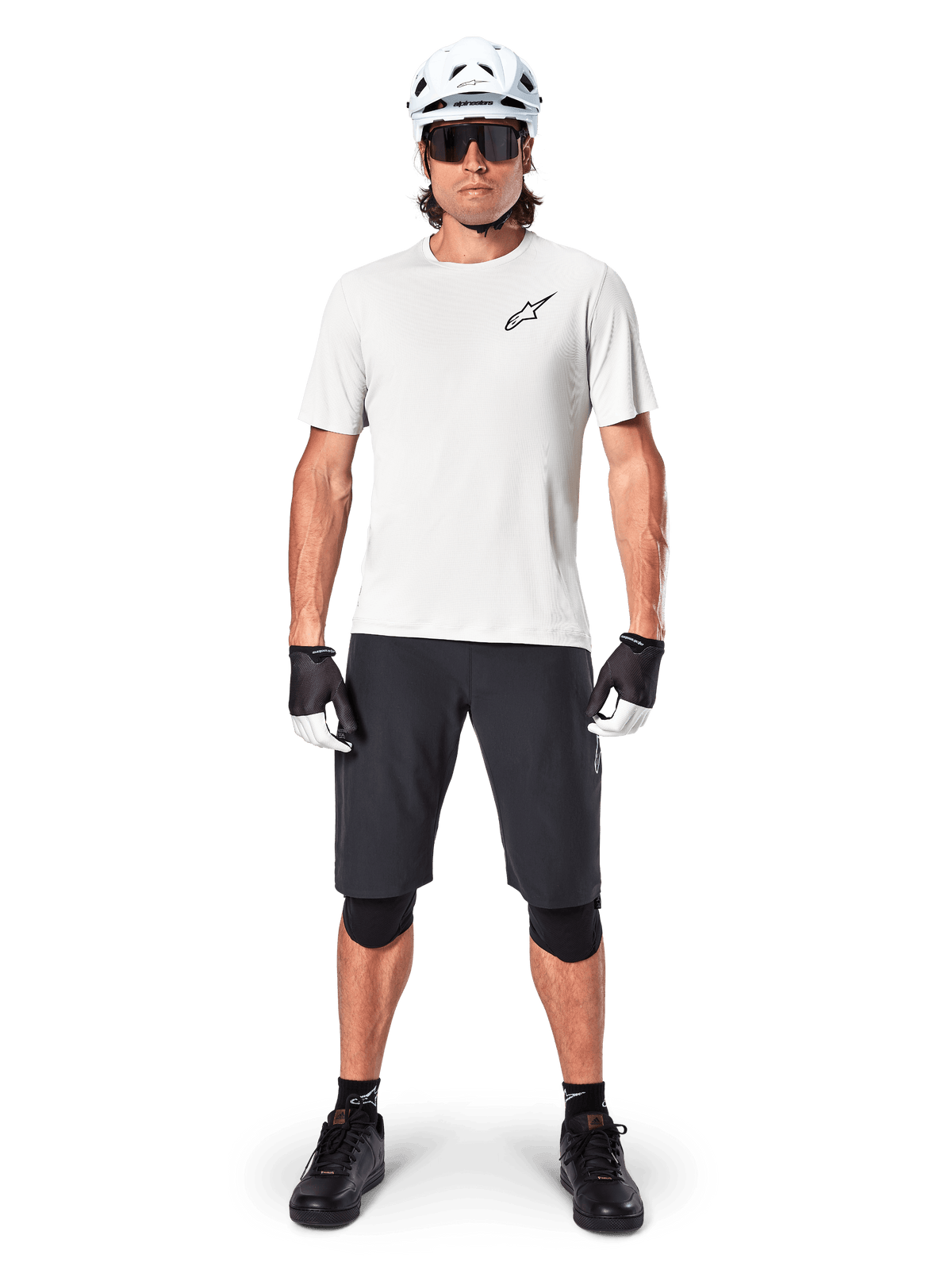 Male mountain biker wearing Alpinestars A-Aria Shorts, Black, paired with a white performance jersey, white helmet, and black knee protectors, professional off-road cycling gear in a full-body front view