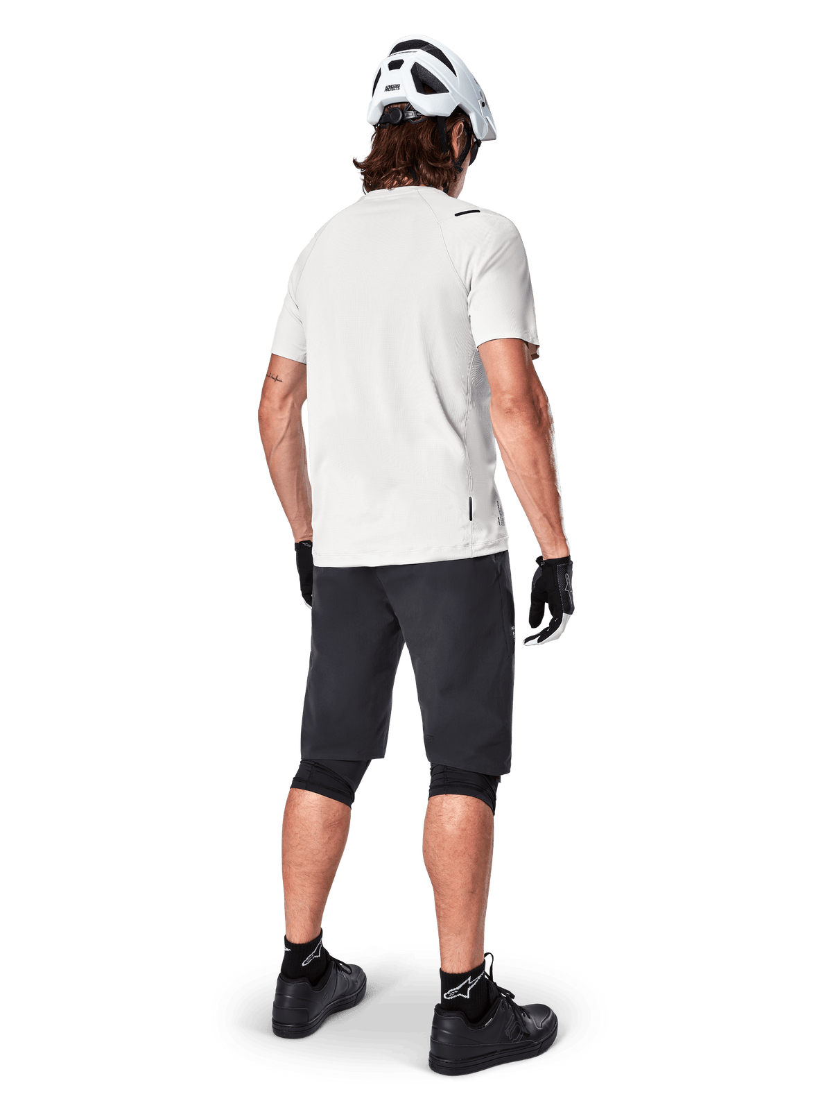 Mountain biker from behind wearing Alpinestars A-Aria Shorts in Black, white performance short-sleeve jersey, white helmet, black gloves, and black mountain bike shoes, cycling gear for trail riding