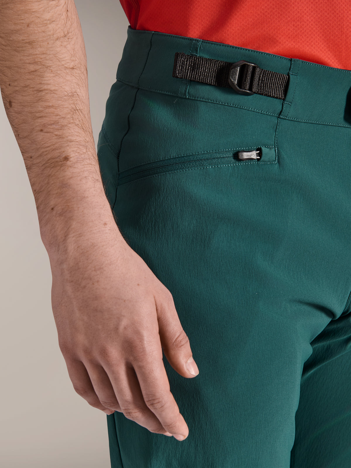 Close-up of Alpinestars A-Dura Pants in Dark Pine green, featuring the adjustable side cinch closure and a zippered mesh-lined pocket, durable mountain bike apparel for off-road trail riding.