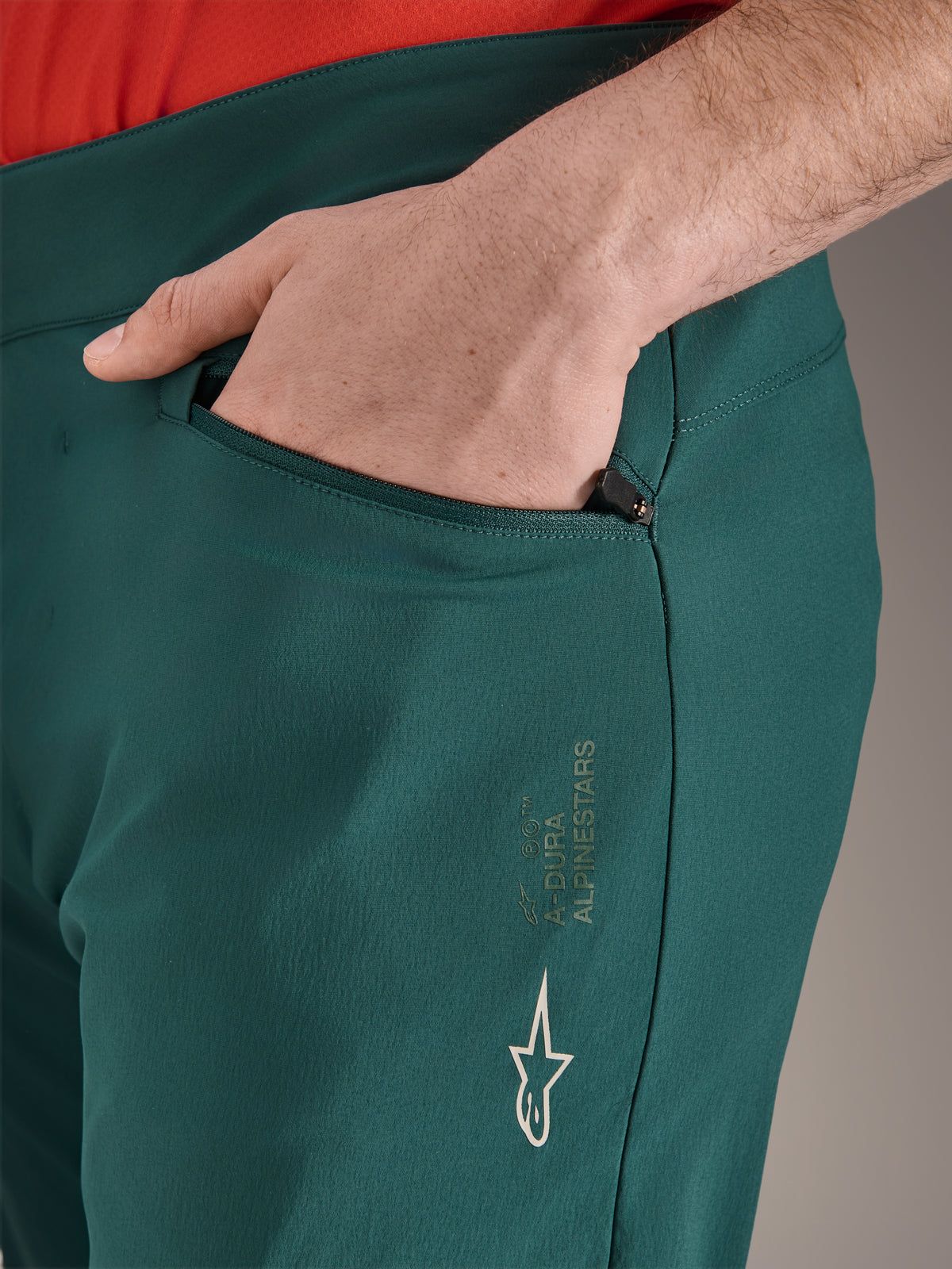 Alpinestars A-Dura Pants in Dark Pine green, close-up of zippered pocket with hand, featuring white Alpinestars logo and text branding on the thigh, durable MTB cycling trousers
