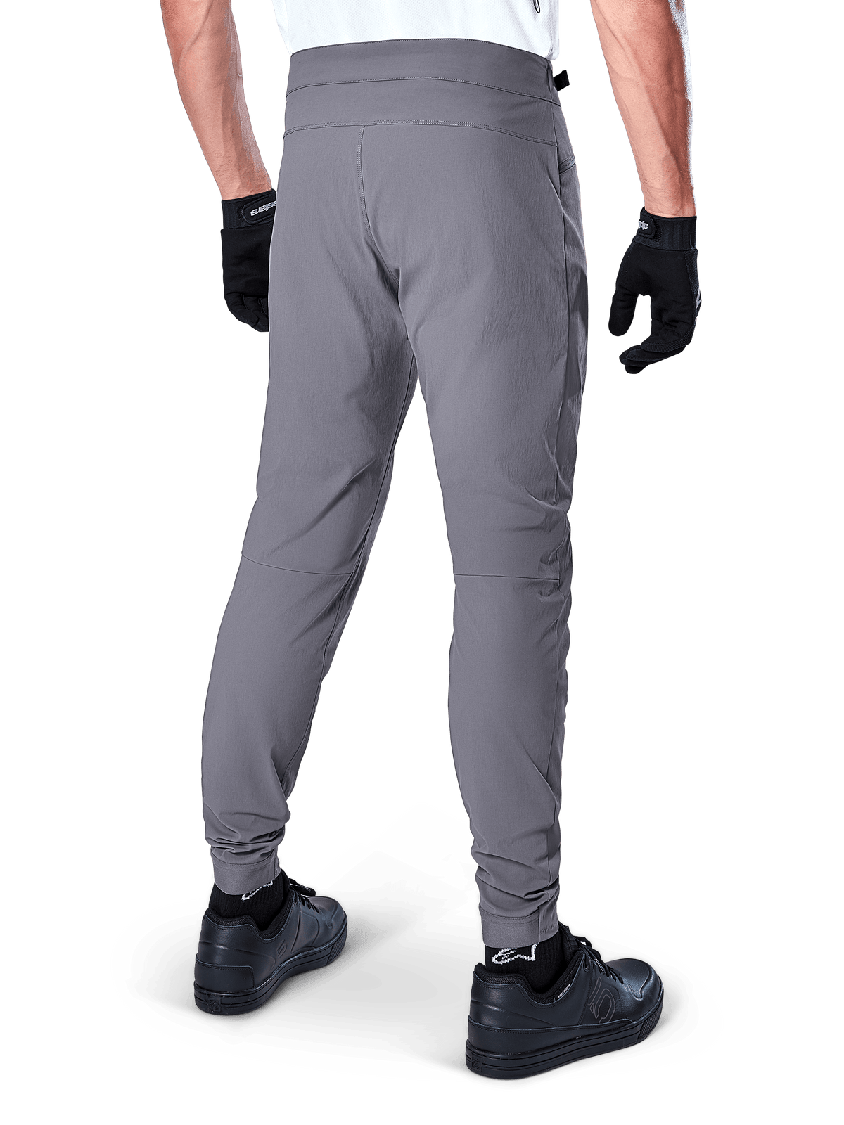 Alpinestars A-Dura Pants, pantalones de bicicleta de montaña, gris oscuro, vista trasera de modelo usando la equipación, con tejido elástico duradero en 2 direcciones y puños elásticos, combinados con guantes y zapatillas negras para un look de ciclismo