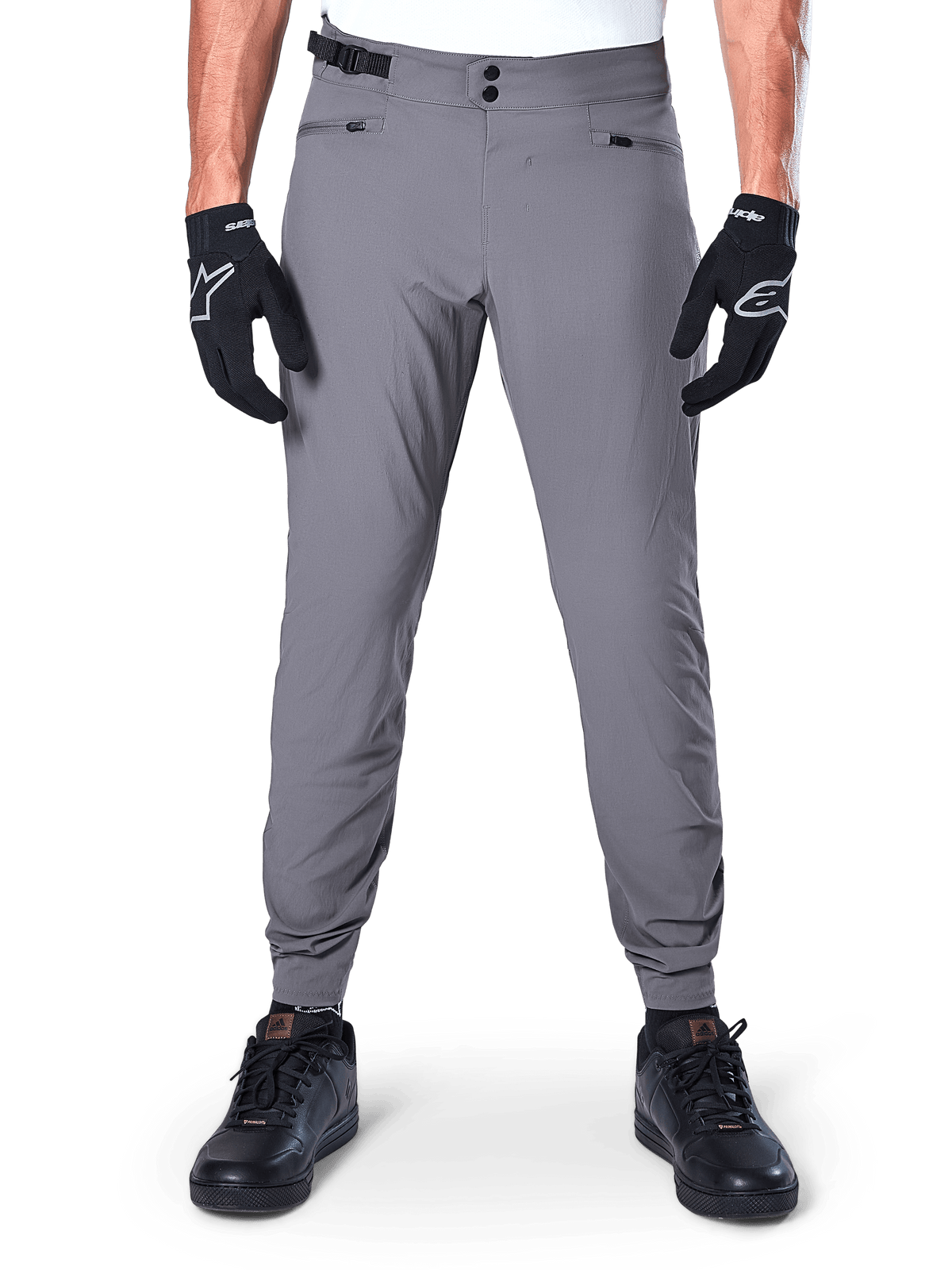Pantalones Alpinestars A-Dura, pantalones de ciclismo de montaña gris oscuro, vista frontal con guantes negros y zapatillas negras, con cierre de cintura de doble broche, bolsillos con cremallera y puños elásticos, ropa de ciclismo duradera para trail riding
