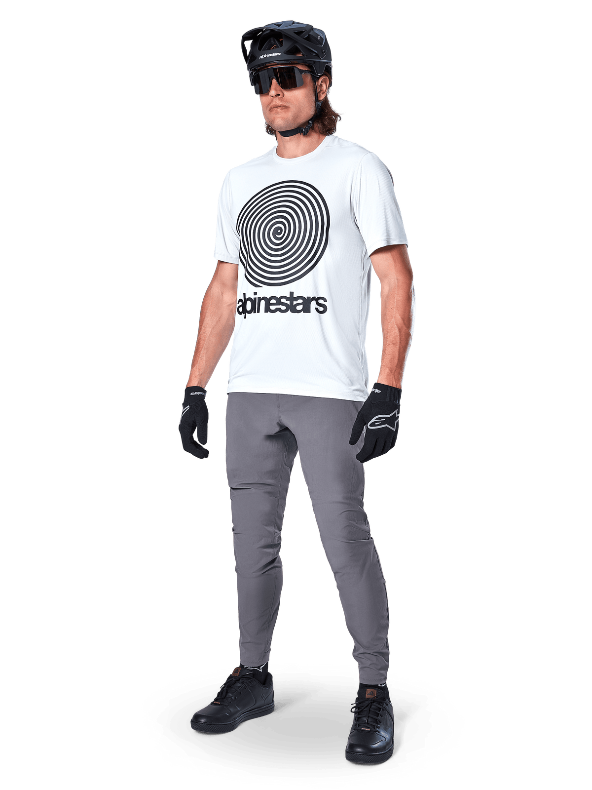 Pantalones Alpinestars A-Dura, pantalones de MTB, gris oscuro, usados con camiseta blanca con gráfico de espiral, casco de MTB negro, gafas de sol y guantes negros, tejido elástico bidireccional duradero para ciclismo todoterreno