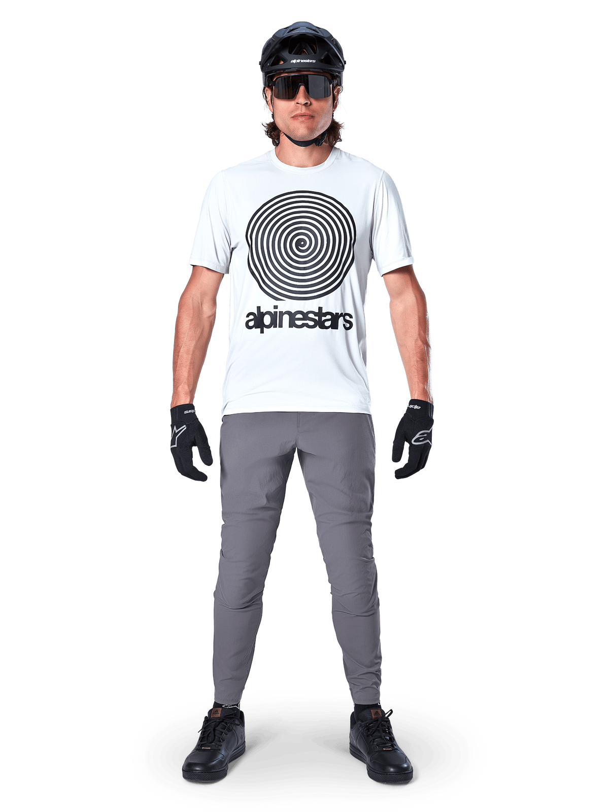 Pantalones Alpinestars A-Dura, pantalones de ciclismo MTB, gris oscuro, combinados con una camiseta blanca con gráfico, casco y guantes negros, con un diseño elástico en 2 direcciones y ajuste regular para ciclismo de montaña