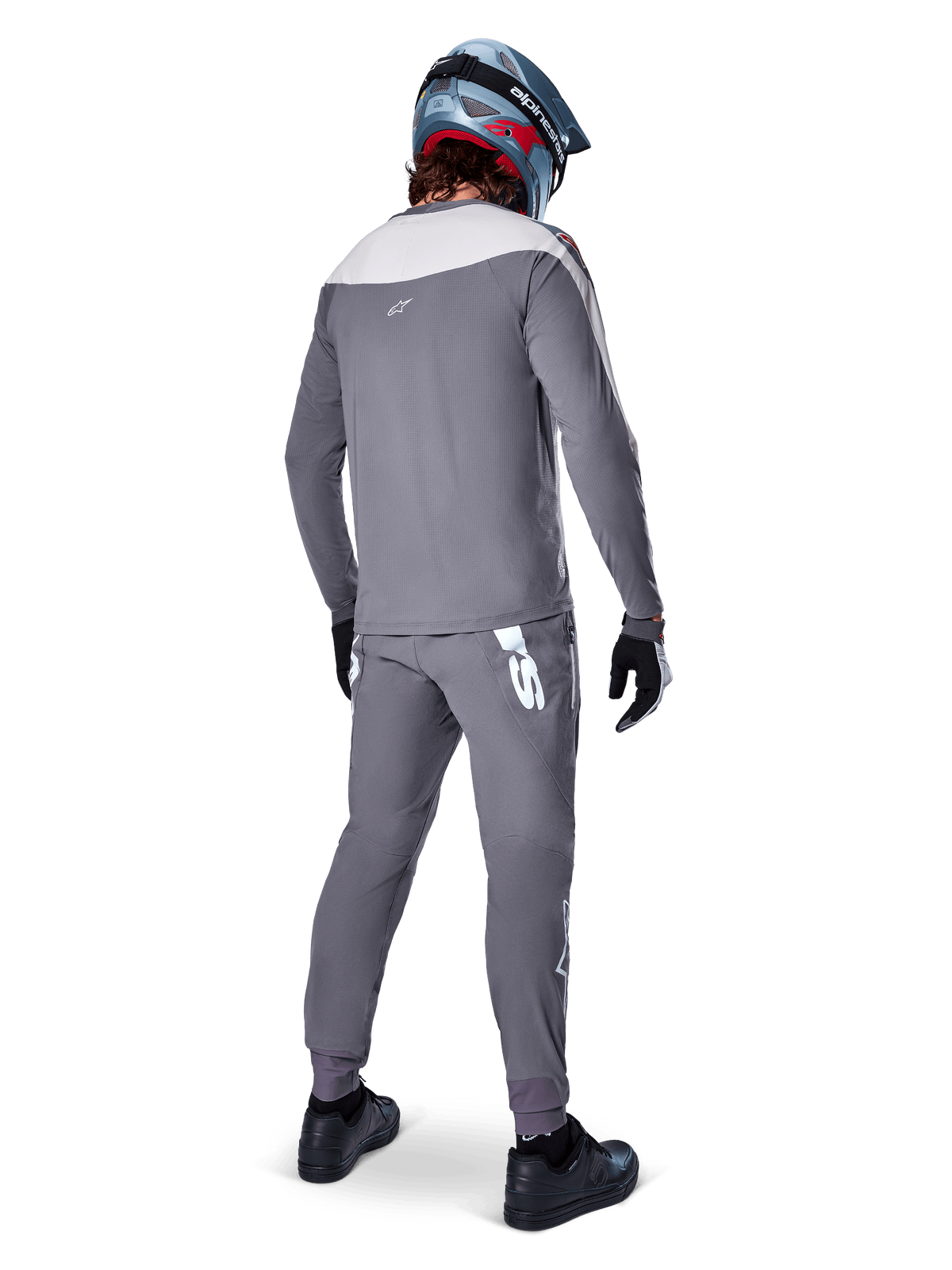 Pantalones Alpinestars A-Supra Race, gris oscuro, ciclista de montaña visto desde atrás con equipamiento de competición completo, jersey gris de manga larga, pantalones gris oscuro con logotipo blanco inspirado en MX en el canesú trasero, casco gris y azul, calzado negro, diseñados para alto rendimiento en MTB