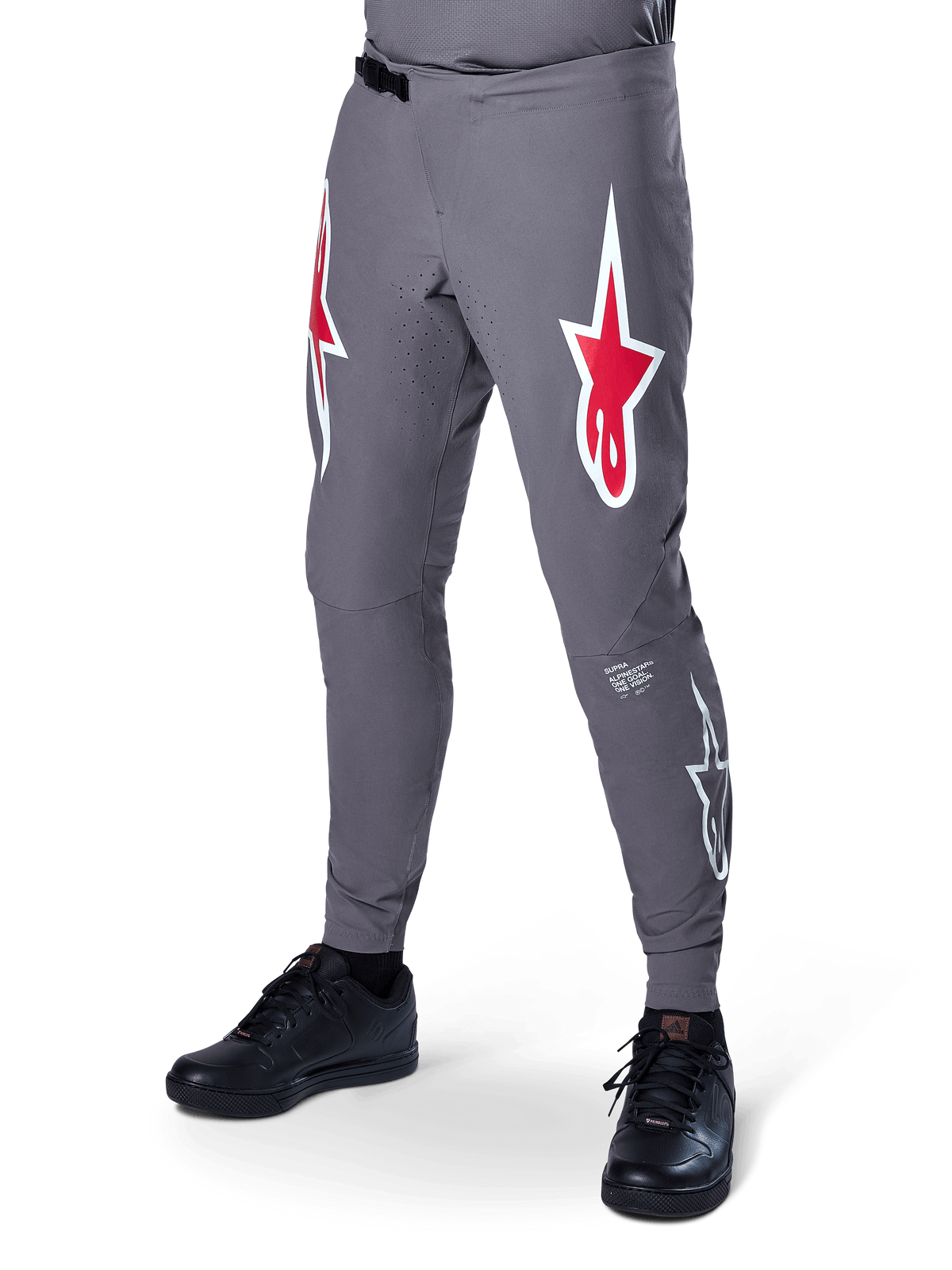 Pantalones Alpinestars A-Supra Race, pantalones de ciclismo de montaña en gris oscuro, con grandes logotipos de estrellas en rojo y blanco en los muslos, ventilación perforada con láser y cierre de cintura con trinquete, ajuste de alto rendimiento para descenso y enduro.