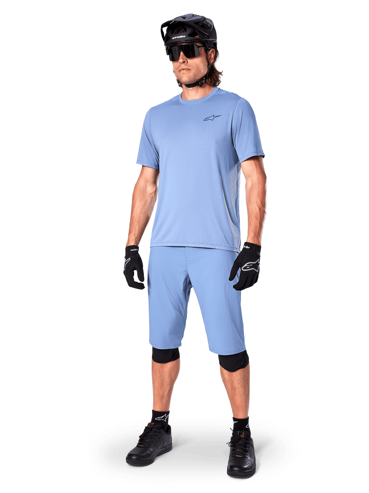 Modelo luciendo los shorts Alpinestars A-Dura en Infinity Blue, jersey de manga corta azul claro a juego, casco de MTB negro, gafas de sol y guantes negros, conjunto completo de ciclismo de montaña para trail