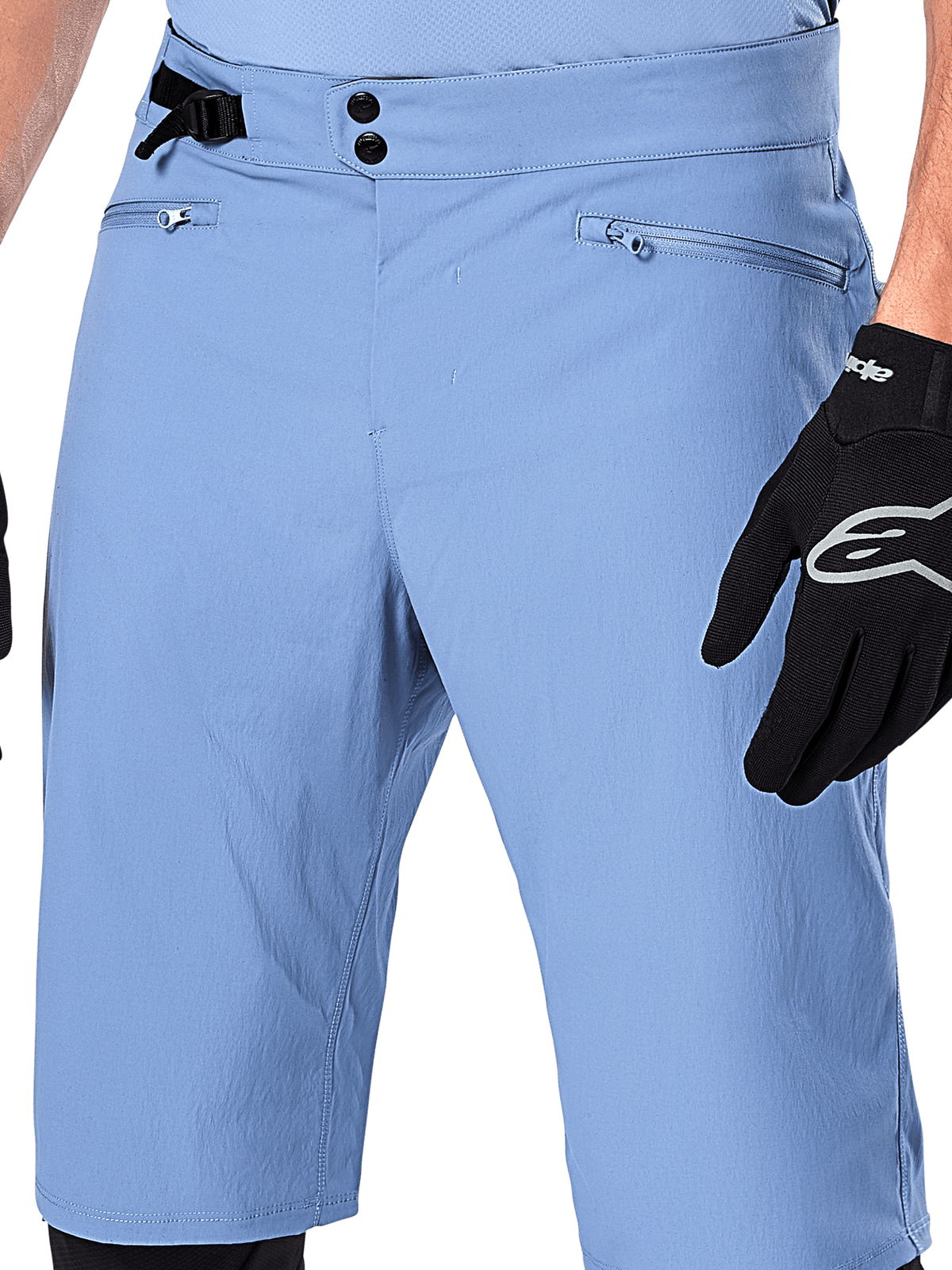Alpinestars A-Dura Shorts, shorts de ciclismo de montaña en color Infinity Blue, primer plano de la cintura con cierre de doble broche, ajuste lateral ajustable y bolsillos con cremallera y forro de malla, usados con un guante Alpinestars negro