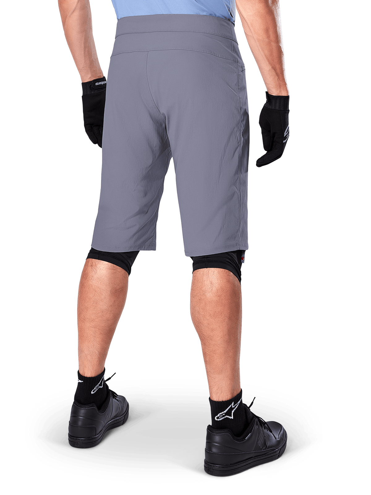Shorts Alpinestars A-Dura, shorts de mountain bike en color gris oscuro, vista trasera mostrada en un ciclista, usados con guantes negros, mallas para rodillas negras y calcetines negros con el logo de Alpinestars, construcción duradera para ciclismo de montaña