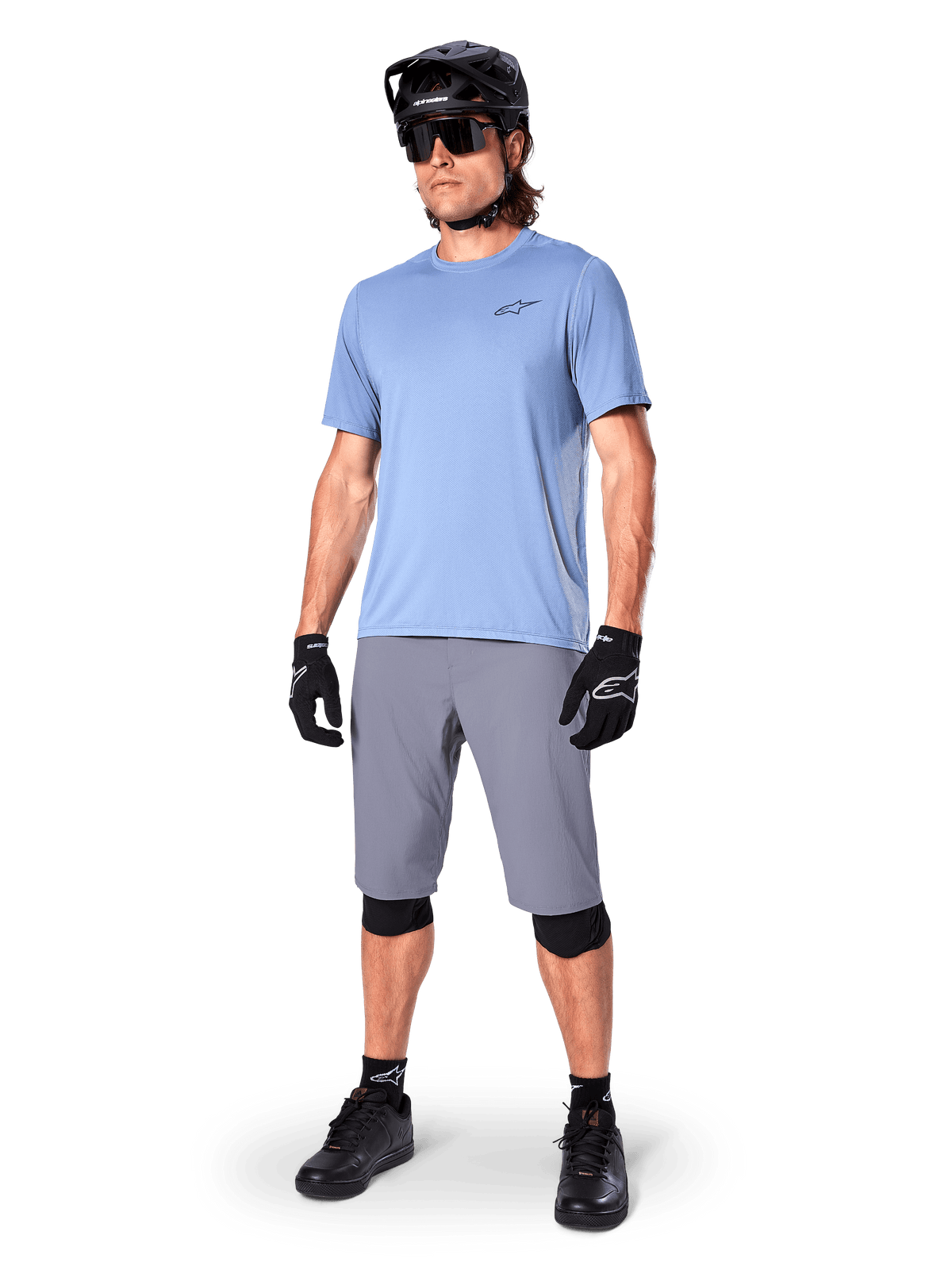 Shorts Alpinestars A-Dura, shorts de MTB, gris oscuro, usados por un ciclista con un jersey azul claro, casco de MTB negro, guantes negros y rodilleras, equipamiento completo de montaña para trail y conducción off-road