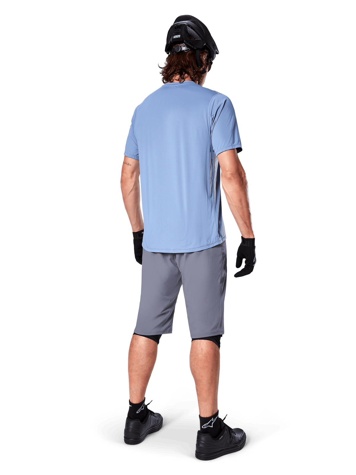 Shorts Alpinestars A-Dura, shorts de MTB en gris oscuro, vista trasera, combinados con un jersey de manga corta azul claro, casco de MTB negro, guantes y calcetines negros con calzado negro, equipamiento funcional y duradero para ciclismo de montaña