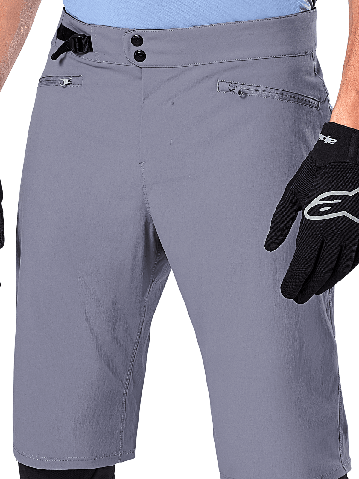 Alpinestars A-Dura Shorts, shorts de MTB, gris oscuro, vista de cerca de la cintura que muestra el cierre de doble broche, ajustador lateral de cintura y bolsillos con cremallera, combinados con guantes de ciclismo negros, ropa duradera para ciclismo de montaña.
