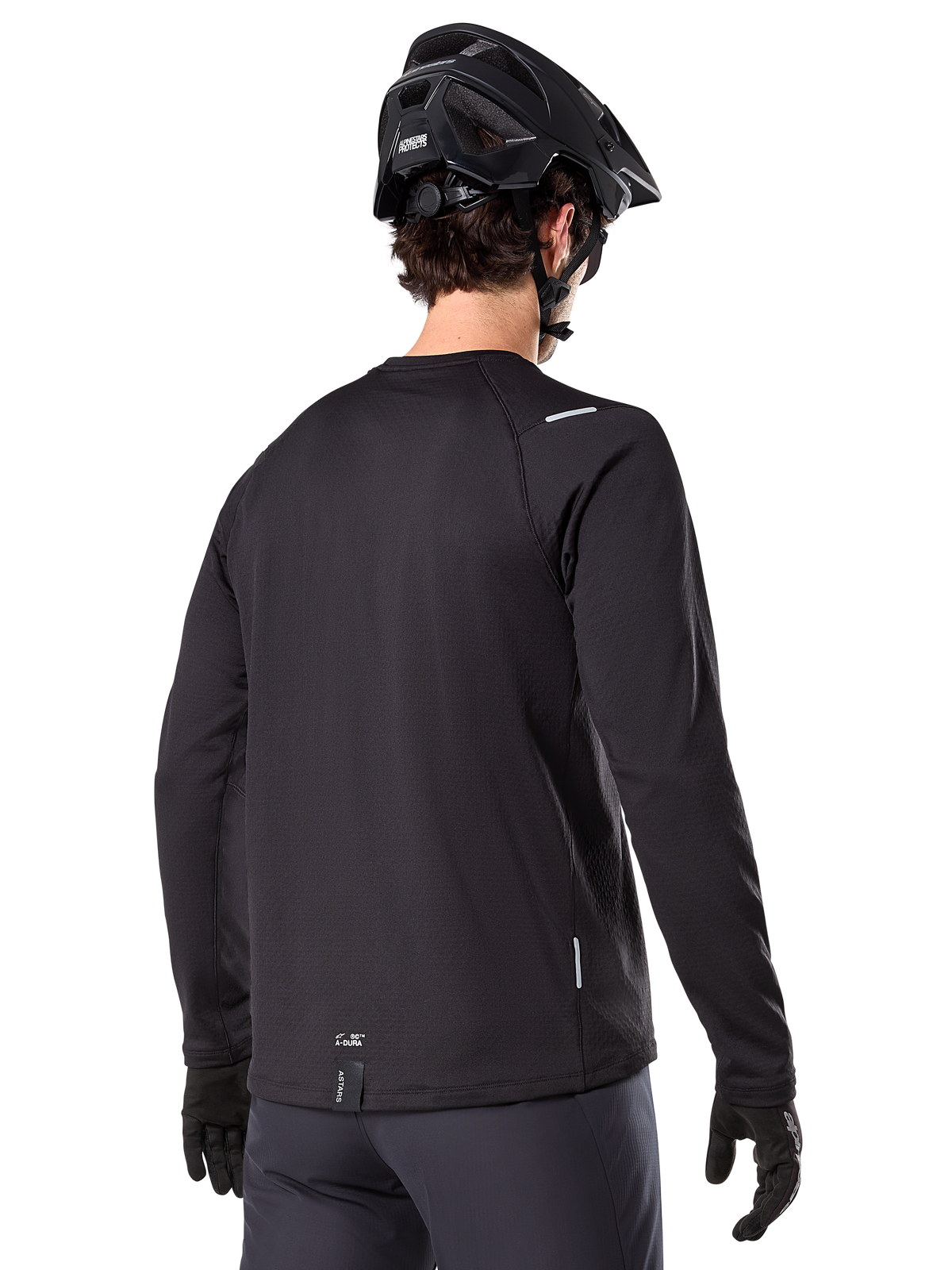 Jersey Térmico Alpinestars A-Dura, jersey de ciclismo de montaña de manga larga, negro, vista trasera que muestra la cola extendida, pequeños detalles reflectantes y logotipo en el dobladillo, usado con un casco y guantes negros para ciclismo en climas fríos
