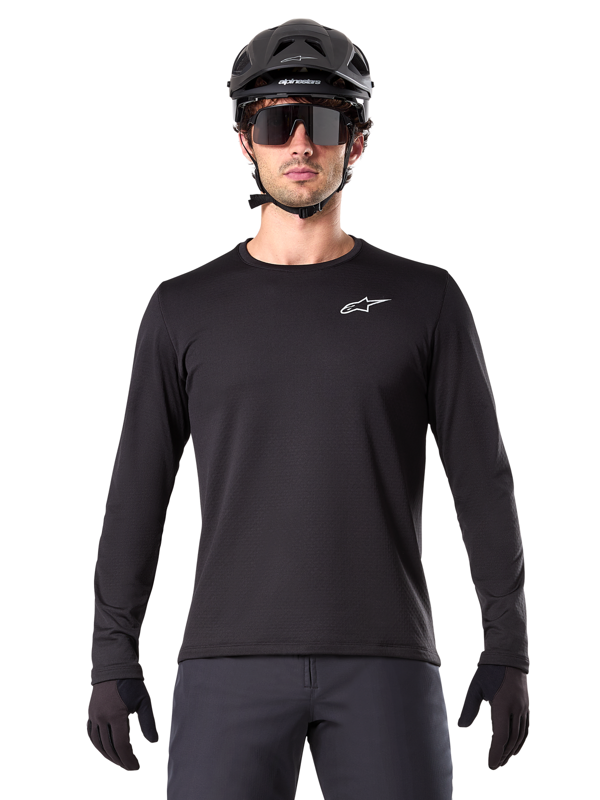 Jersey Térmico Alpinestars A-Dura, jersey de ciclismo de montaña de manga larga en color negro, usado con casco negro y gafas de sol grandes, con un pequeño logotipo blanco de Alpinestars en el pecho, ajuste regular, ropa de ciclismo MTB