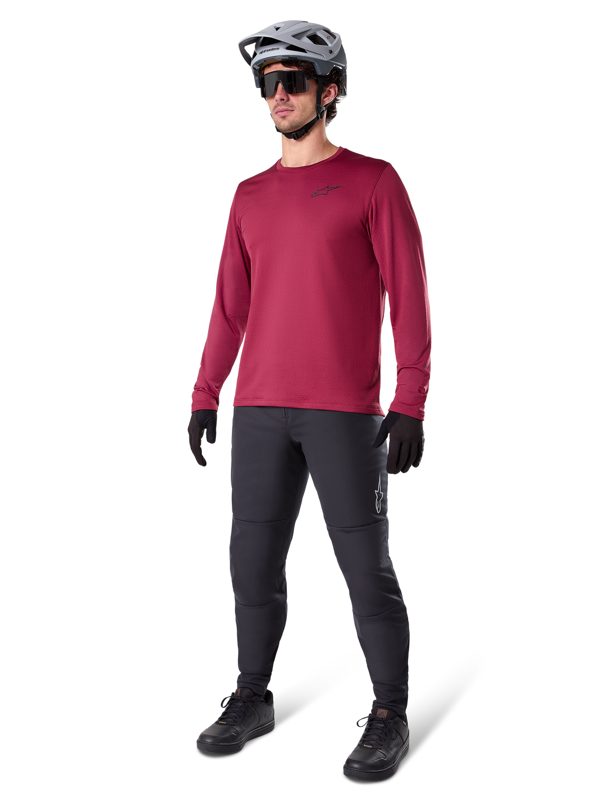 Jersey térmico Alpinestars A-Dura en color granate, camiseta de ciclismo aislante de manga larga combinada con pantalones de ciclismo de montaña gris oscuro, guantes negros y casco gris, toma de estudio de cuerpo completo de equipamiento de MTB para clima frío.
