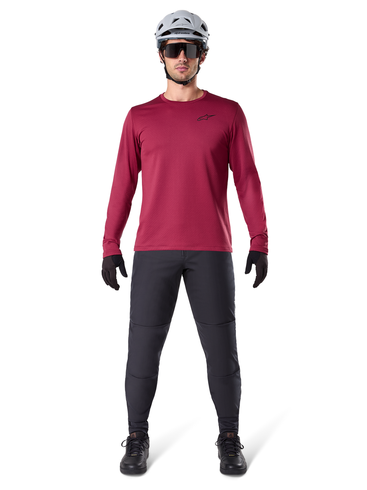 Modelo masculino vistiendo el Jersey Térmico Alpinestars A-Dura en color borgoña, camiseta técnica de ciclismo de manga larga con aislamiento, combinada con pantalones de MTB gris oscuro, casco blanco, gafas de sol negras y guantes negros, equipamiento profesional de MTB para clima frío