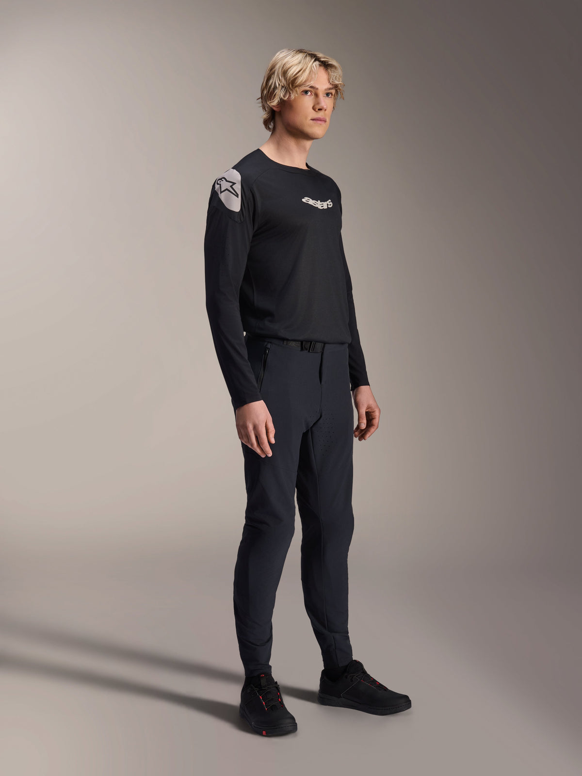 Model wearing Alpinestars A-Aria Polartec Elite Long Sleeve Jersey in Black, paired with matching black technical mountain bike pants and black shoes, performance cycling apparel for off-road riding, studio shot.