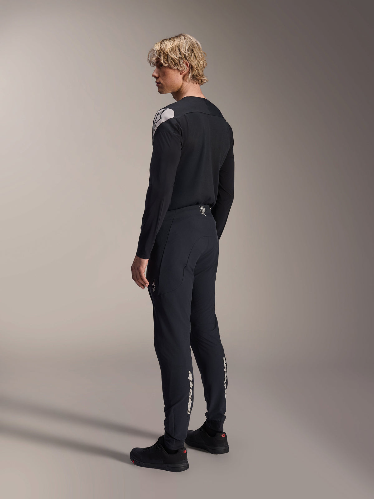 Alpinestars A-Aria Polartec Elite Jersey - Long Sleeve, Black, worn by a model from a back-side profile, featuring a white logo on the shoulder, paired with matching black cycling pants for a professional MTB outfit.