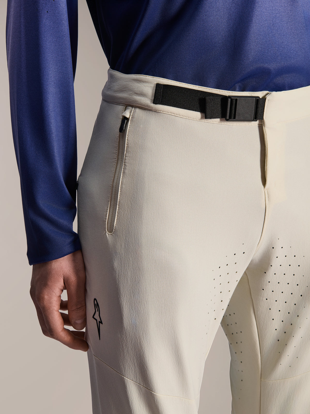Alpinestars A-Aria Elite Pants, Mountain Bike Pants, Ecru, close-up featuring a black magnetic buckle waist closure, zippered pocket, and laser-cut ventilation holes, performance off-road cycling gear.