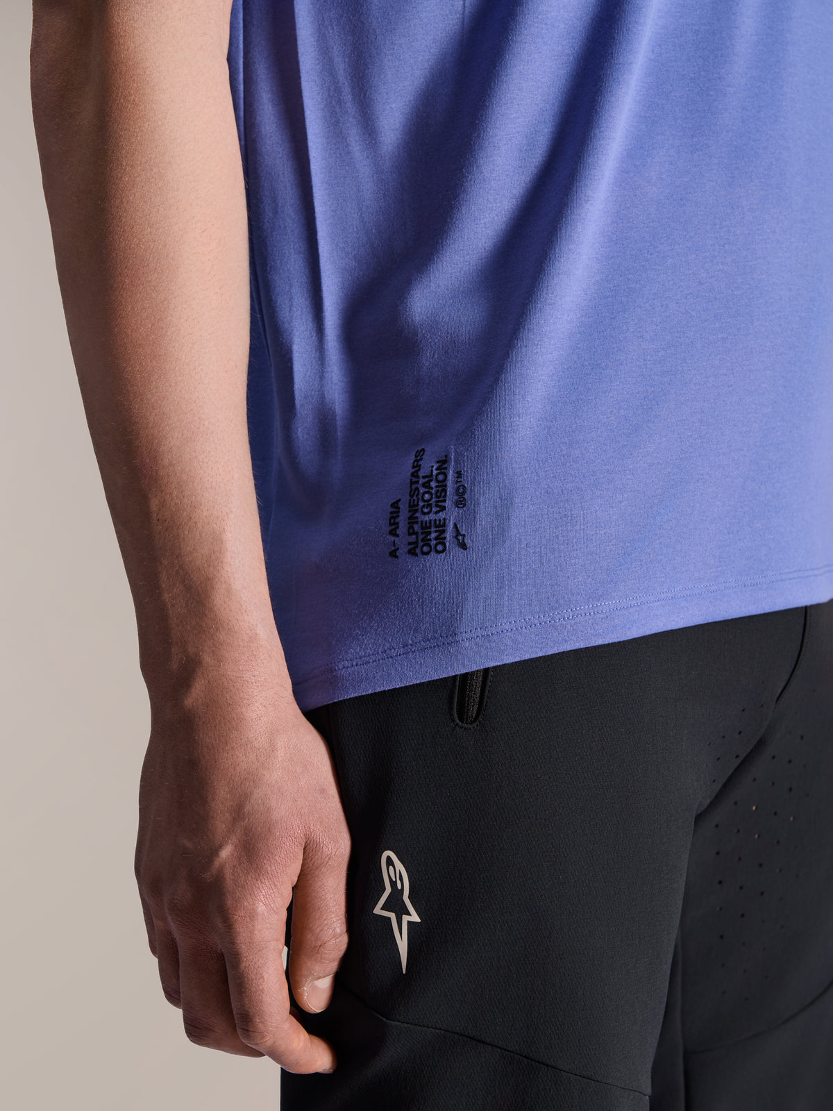 Jersey de manga corta Alpinestars A-Aria Polartec Elite en color Baja Blue, detalle del dobladillo lateral inferior con el texto 'One Goal. One Vision.' en negro y el logotipo ASTARS, combinado con pantalones cortos negros de bicicleta de montaña.